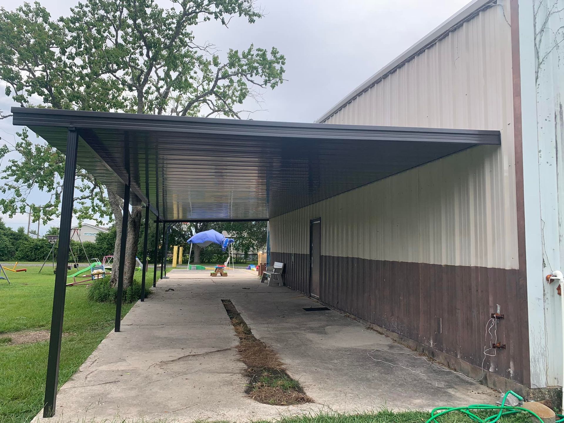 Covered concrete walkway beside a large metal building on a cloudy day