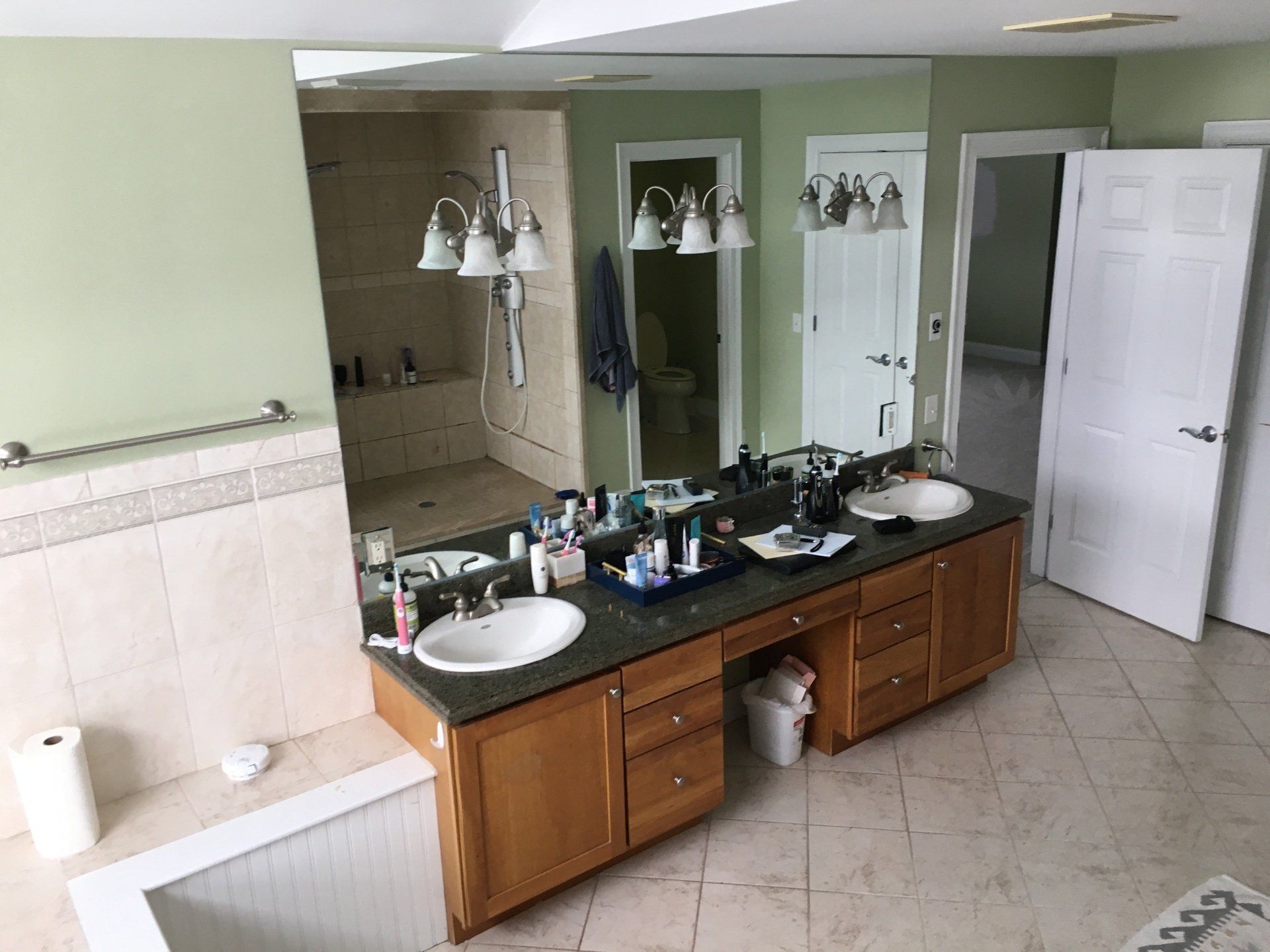 Bathroom with double wooden vanity, large mirrors, white sinks, and green walls.