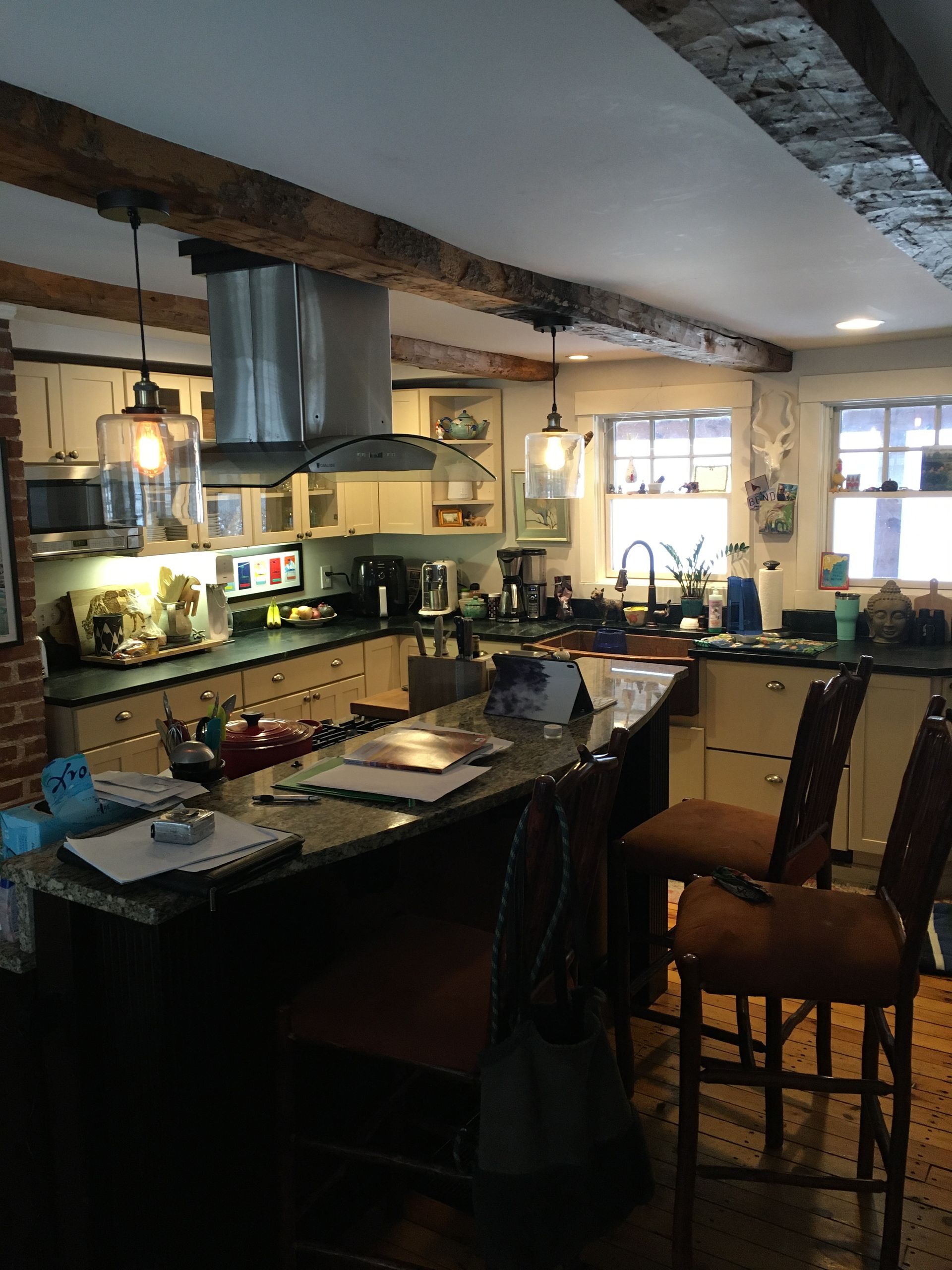 Cozy kitchen with black counters, hanging lights, exposed beams, and a window over the sink