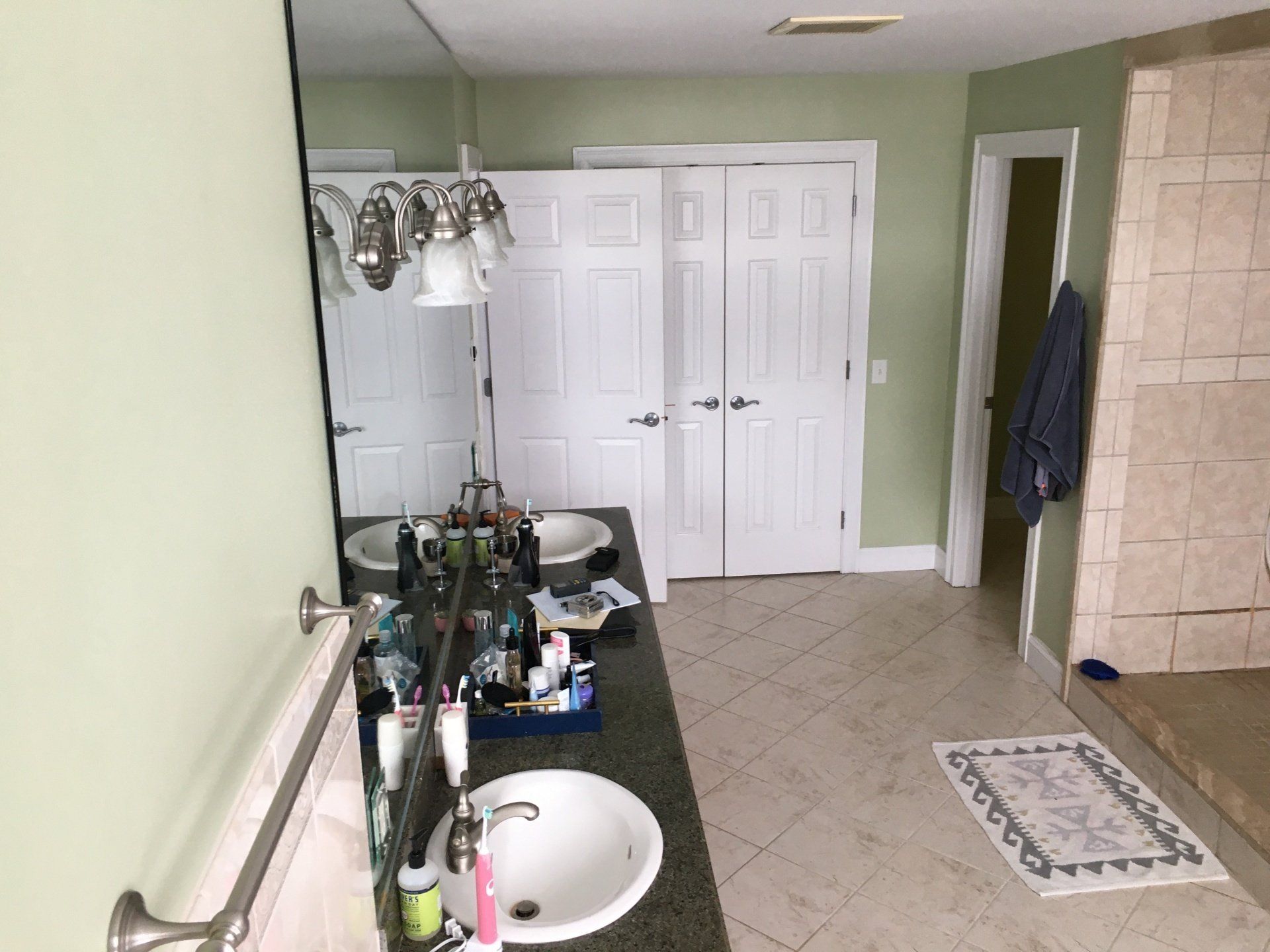 Bathroom with green walls, tiled floor, vanity sink, mirrors, and white double closet doors.