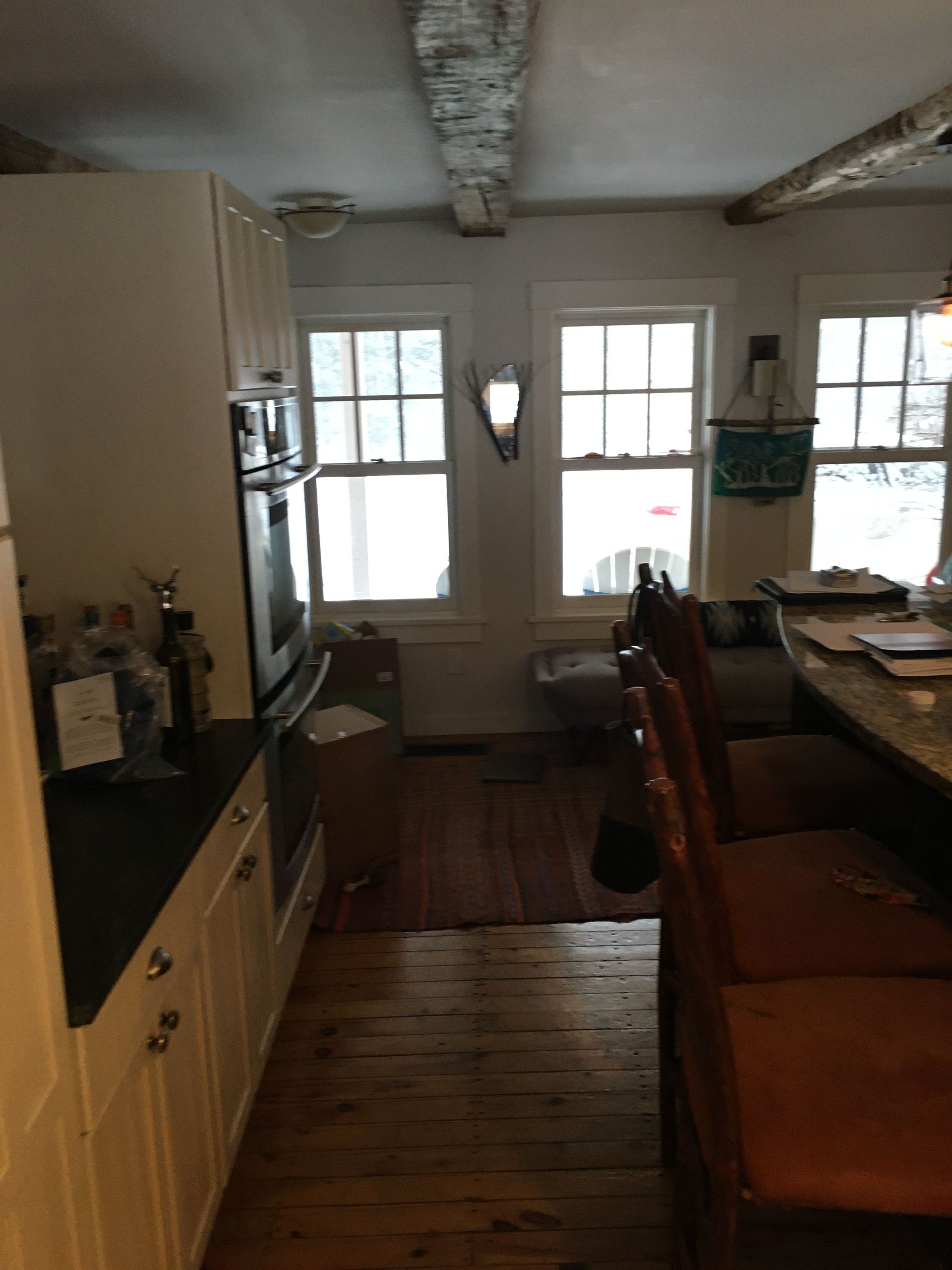 A rustic kitchen with wooden floors, white cabinets, and a dining table by bright windows.