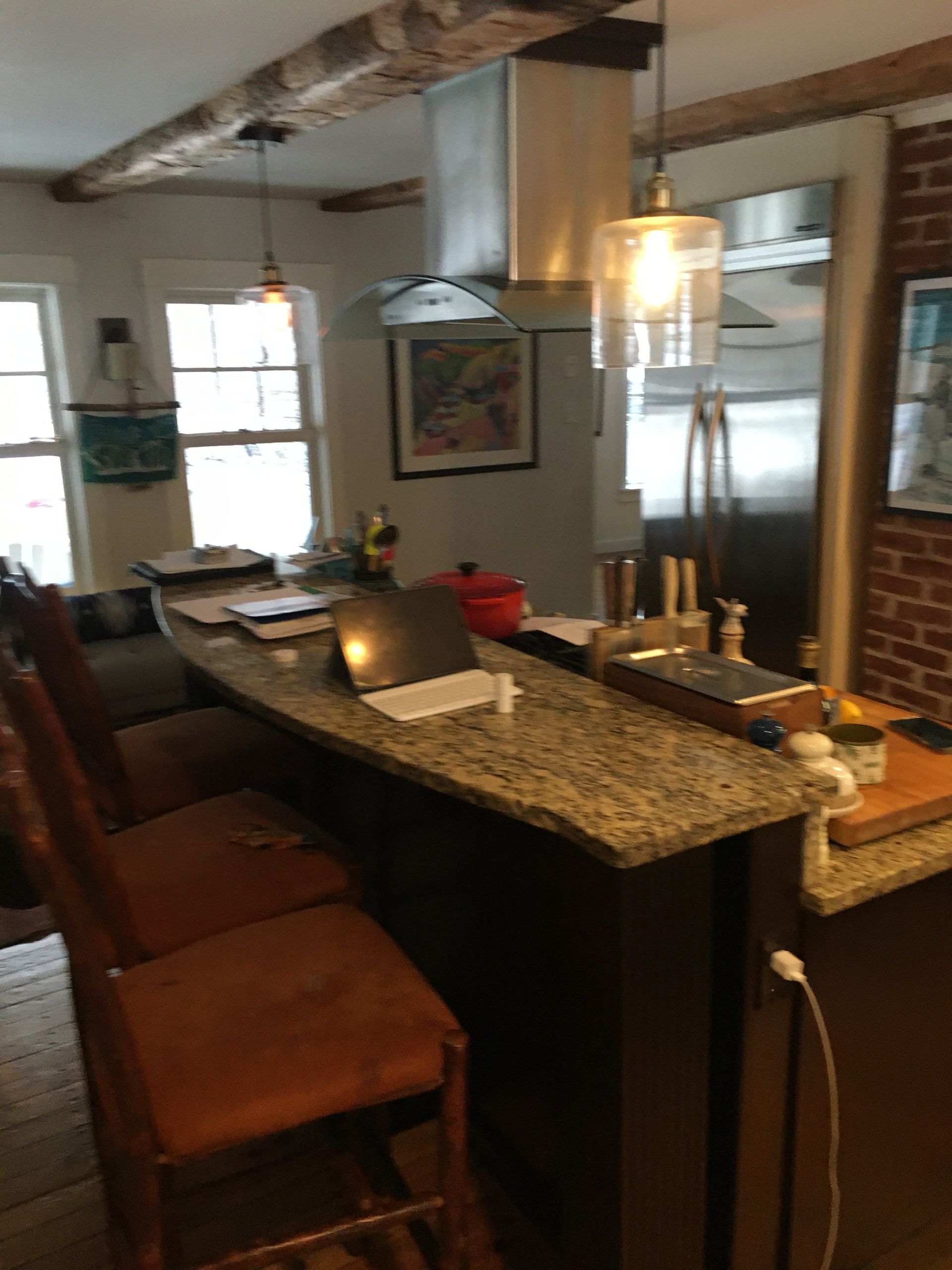 Modern kitchen with granite island, pendant lights, and brick walls; stools line the counter.