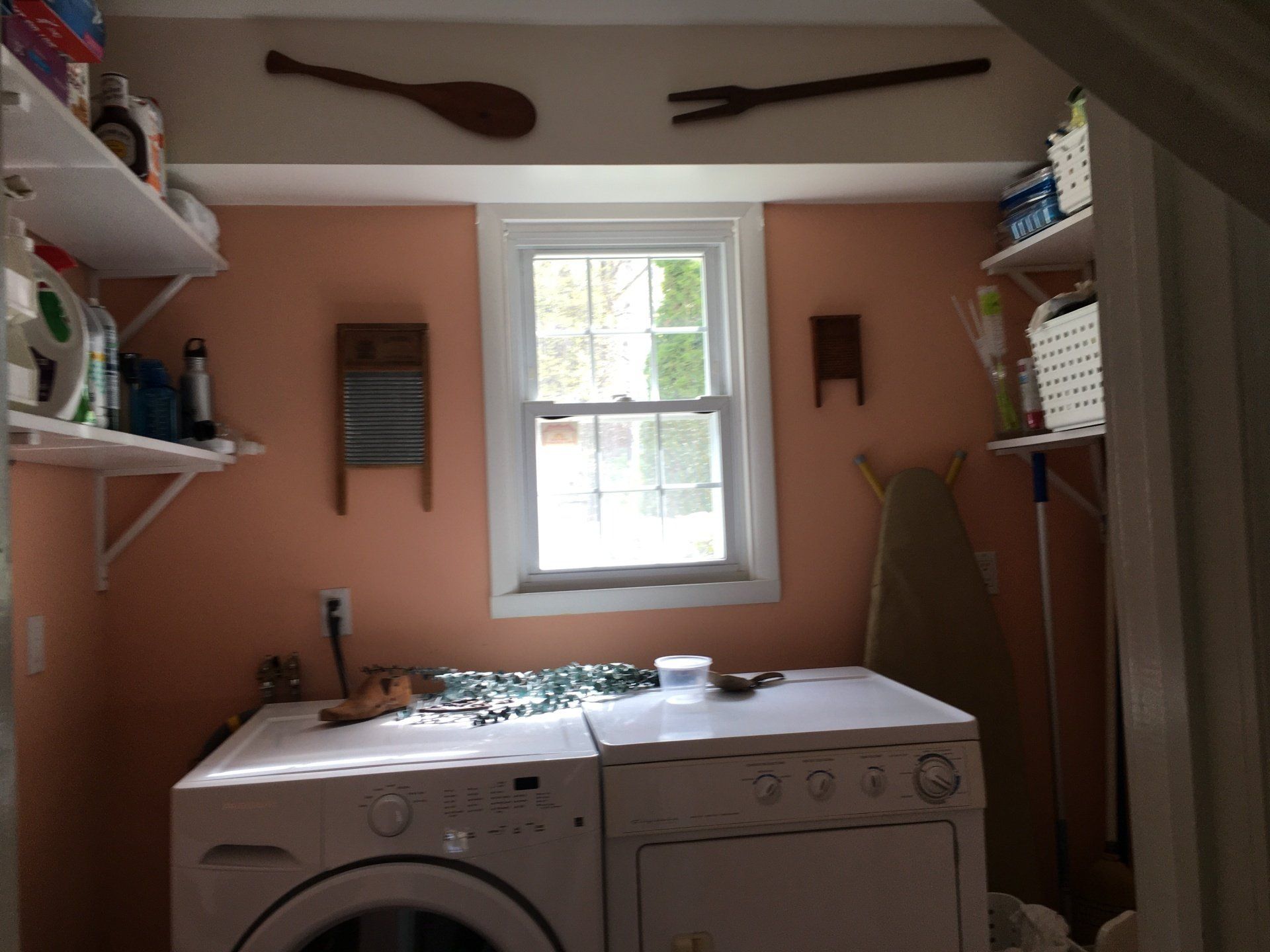 Laundry room with washer and dryer under a window, shelves, and cleaning supplies on peach walls