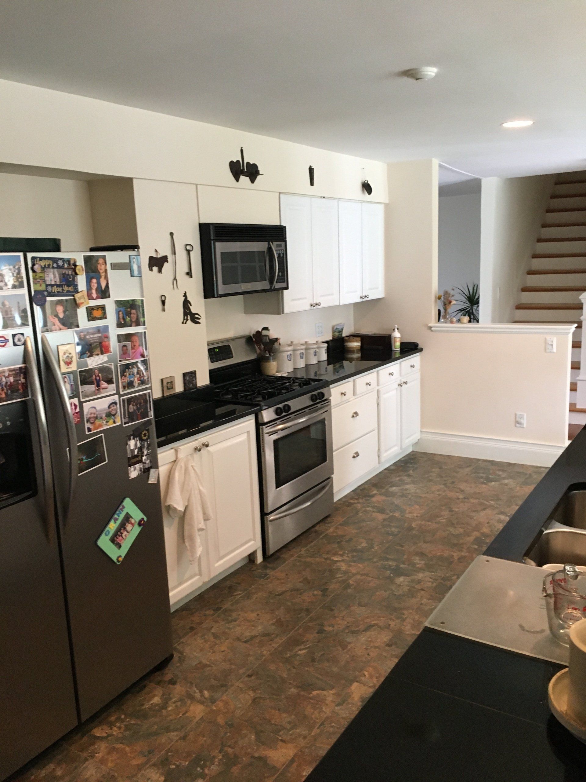 Modern kitchen with black refrigerator, stainless stove, white cabinets, and stairs in the background