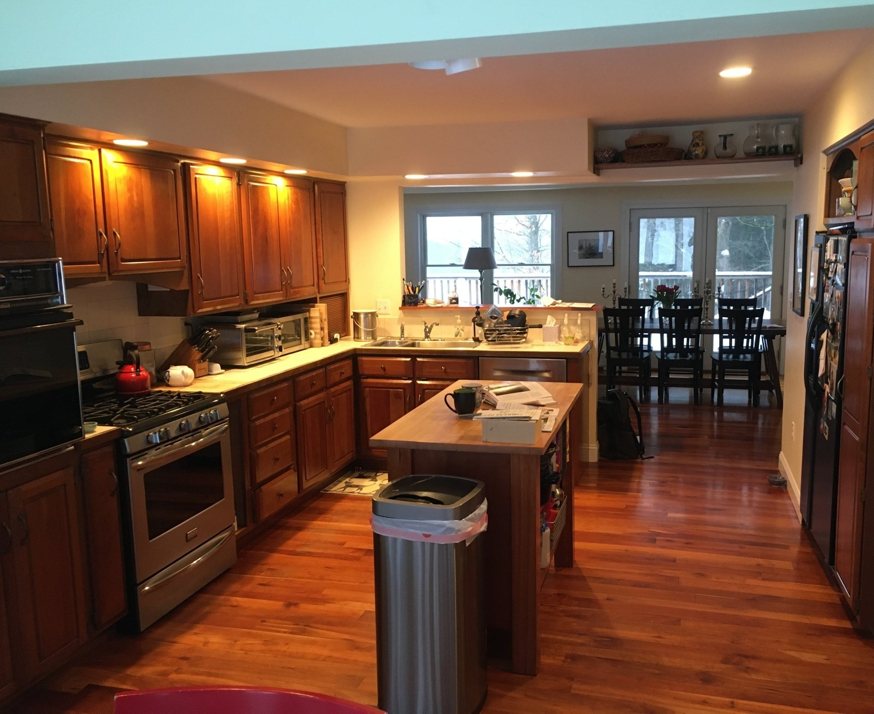 Warm kitchen with wooden cabinets, stainless stove, central island, and open view to a dining area.