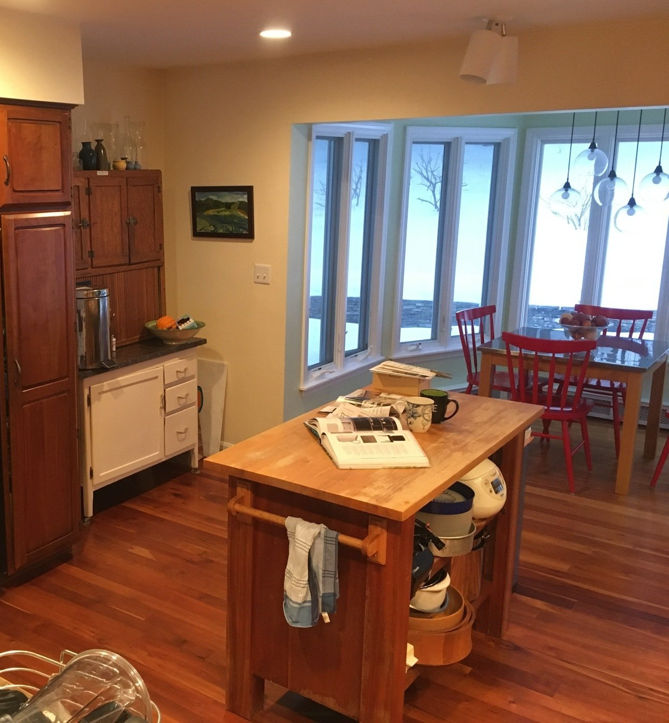Kitchen with wood floors, island counter, and red dining chairs by a bright bay window.