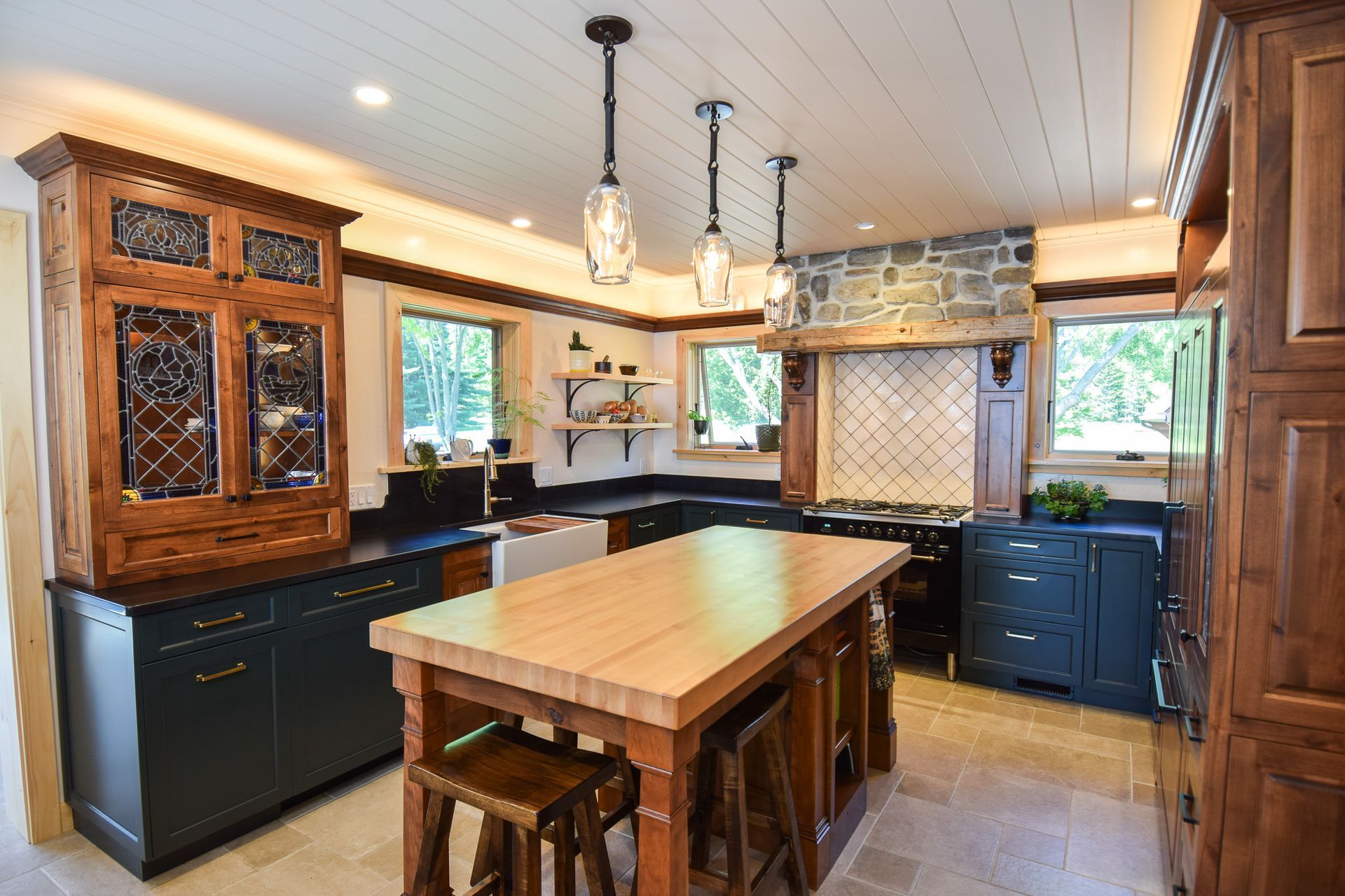 Warm rustic kitchen with wooden island, dark cabinets, hanging lights, and large windows