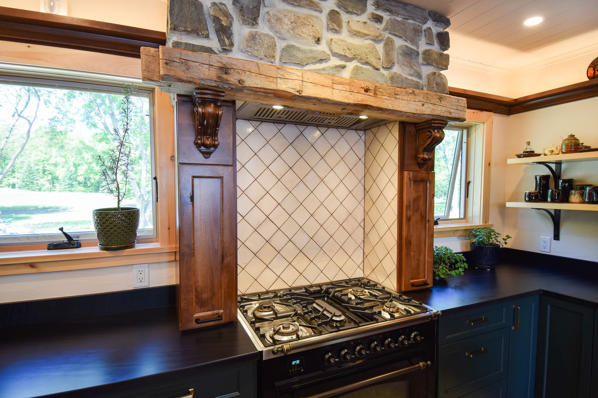 Kitchen range beneath stone hood with tiled backsplash, dark counters, and window shelves