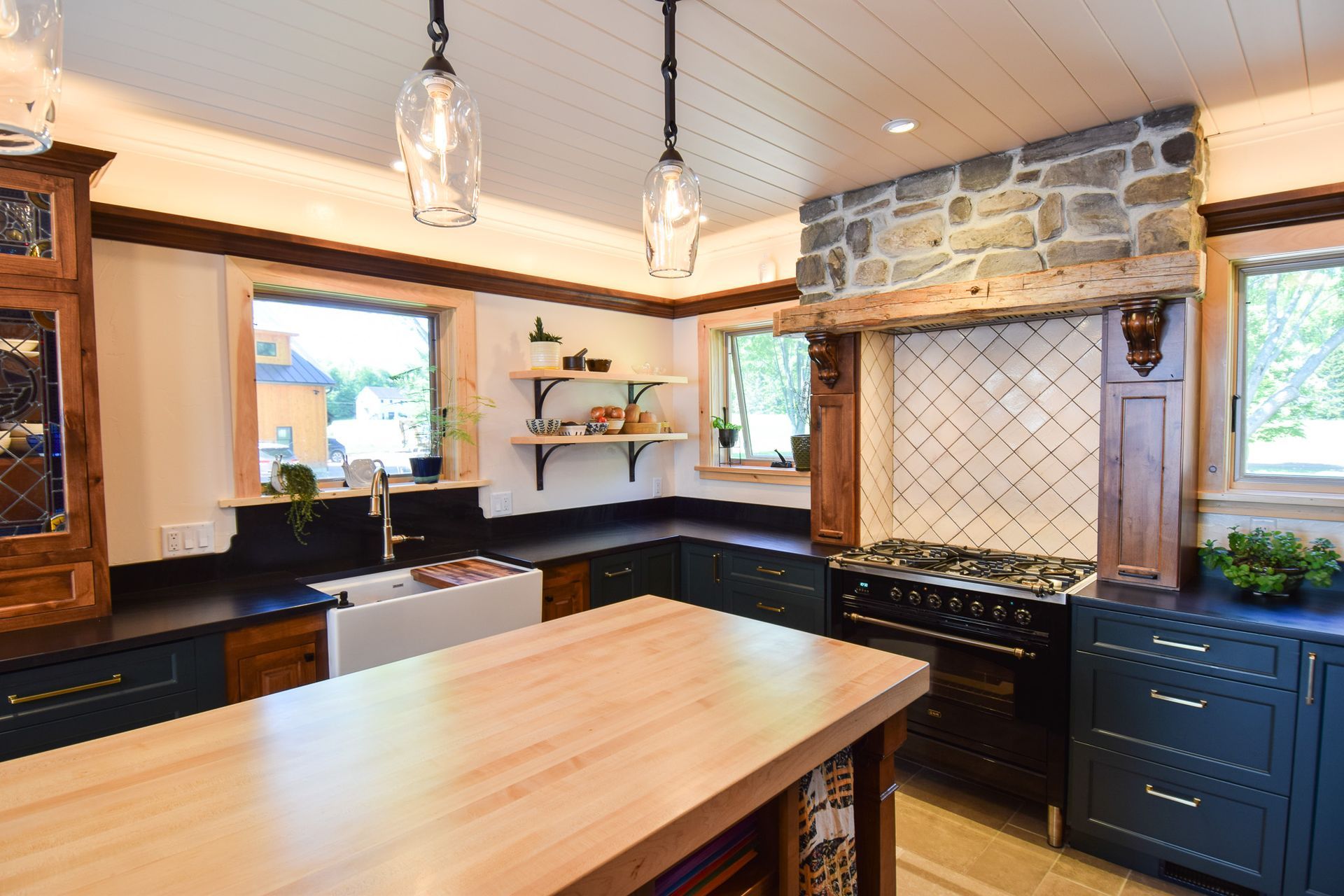 Modern rustic kitchen with wood island, black cabinets, stone fireplace, and hanging pendant lights
