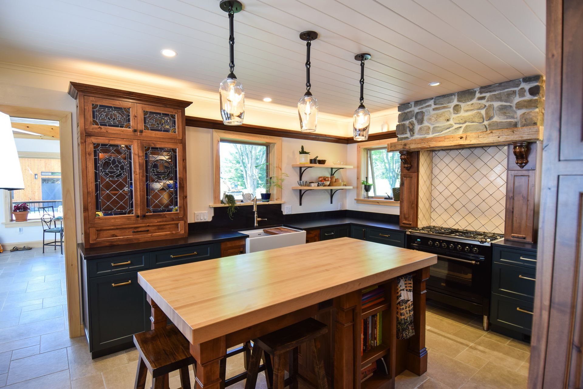 Modern kitchen with a large wooden island, black cabinets, stone backsplash, and pendant lights