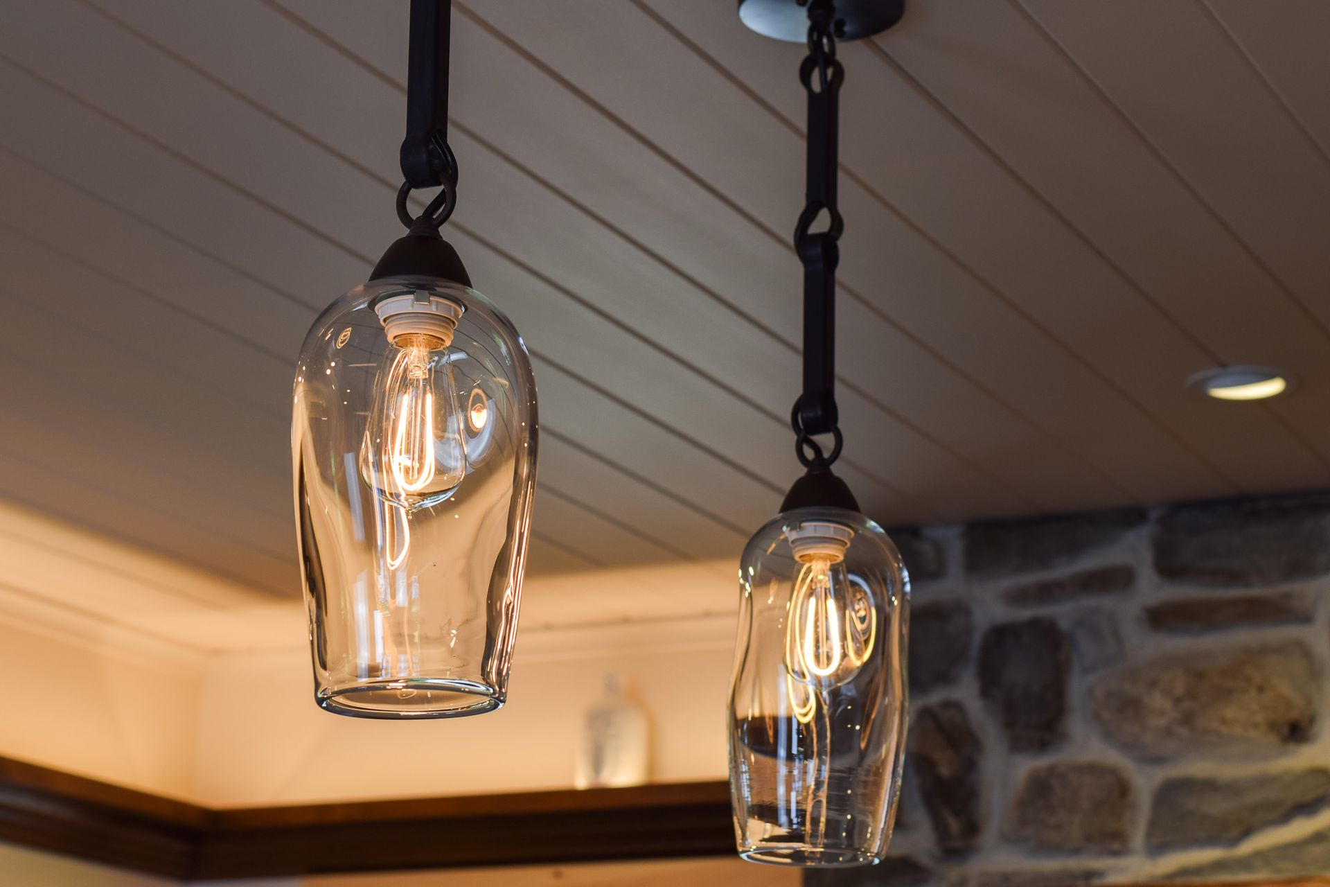 Two hanging glass pendant lights with exposed bulbs over a wood ceiling