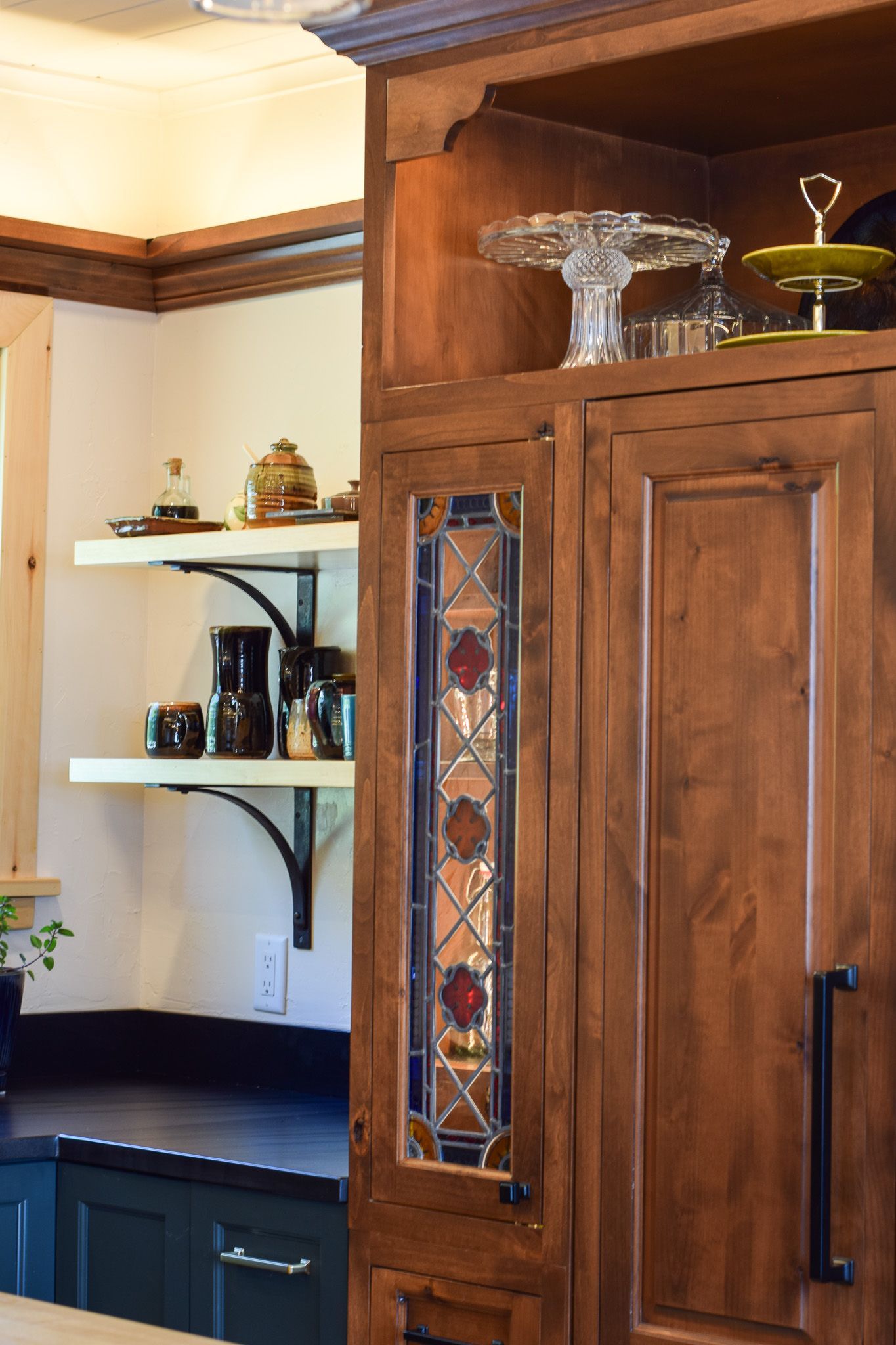 Wooden kitchen cabinet with stained glass panel beside open shelves and dark countertops