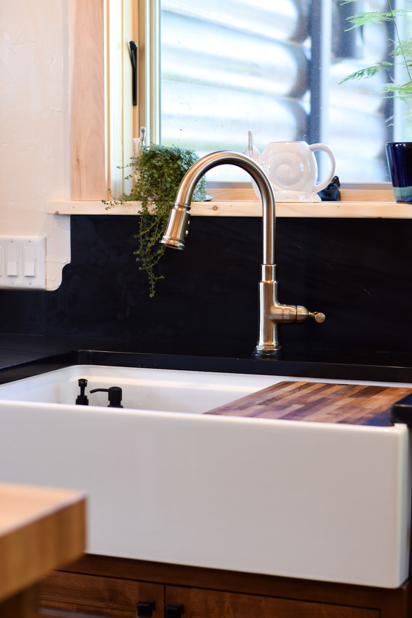 Modern kitchen sink with high-arc faucet, white basin, black backsplash, and window light