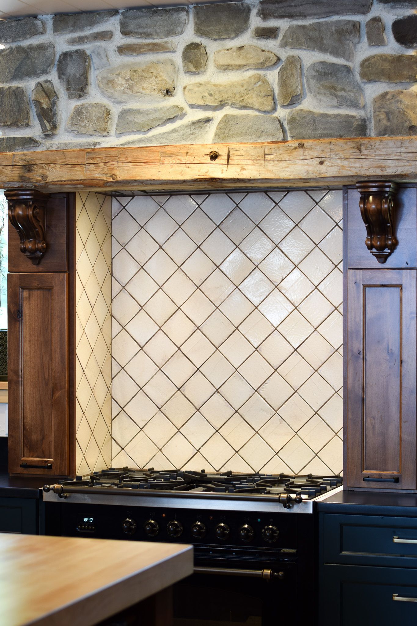 Stone-wall kitchen with wood range hood, cream tile backsplash, and black stove under a cabinet niche