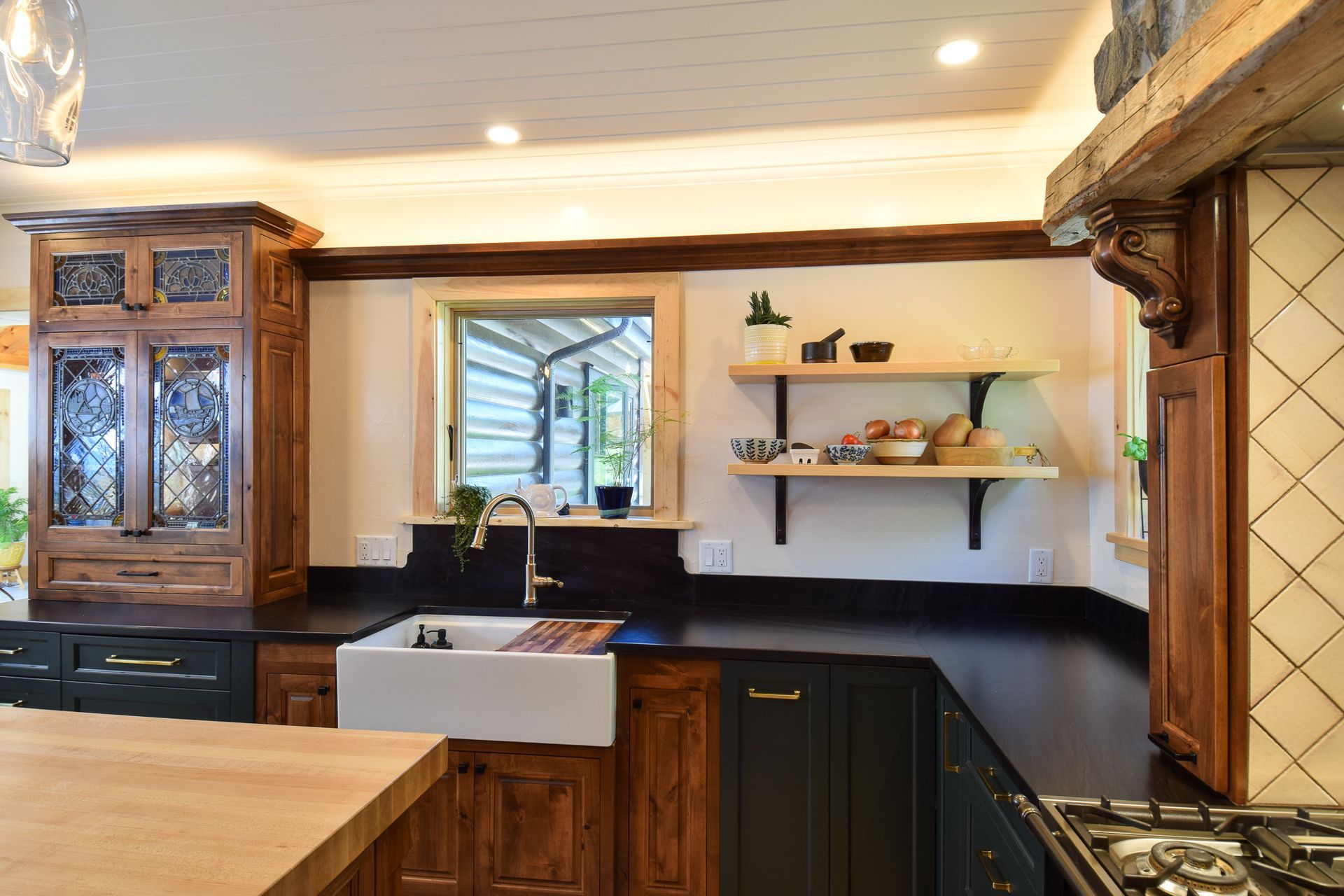 Warm wood kitchen with black counters, white farmhouse sink, and open shelves by a window