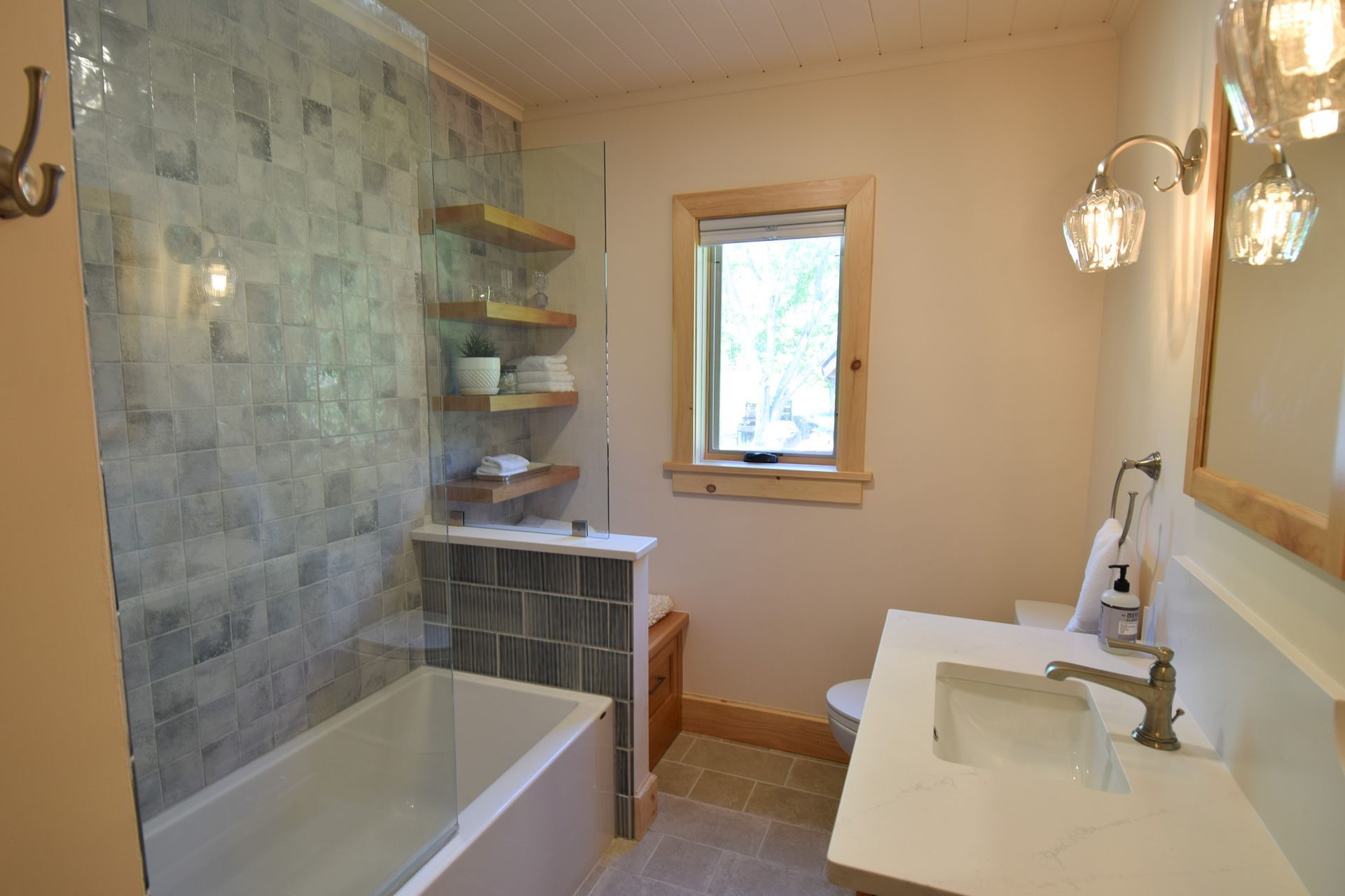 Bathroom with tiled shower-tub, vanity sink, wood mirror, and small window.