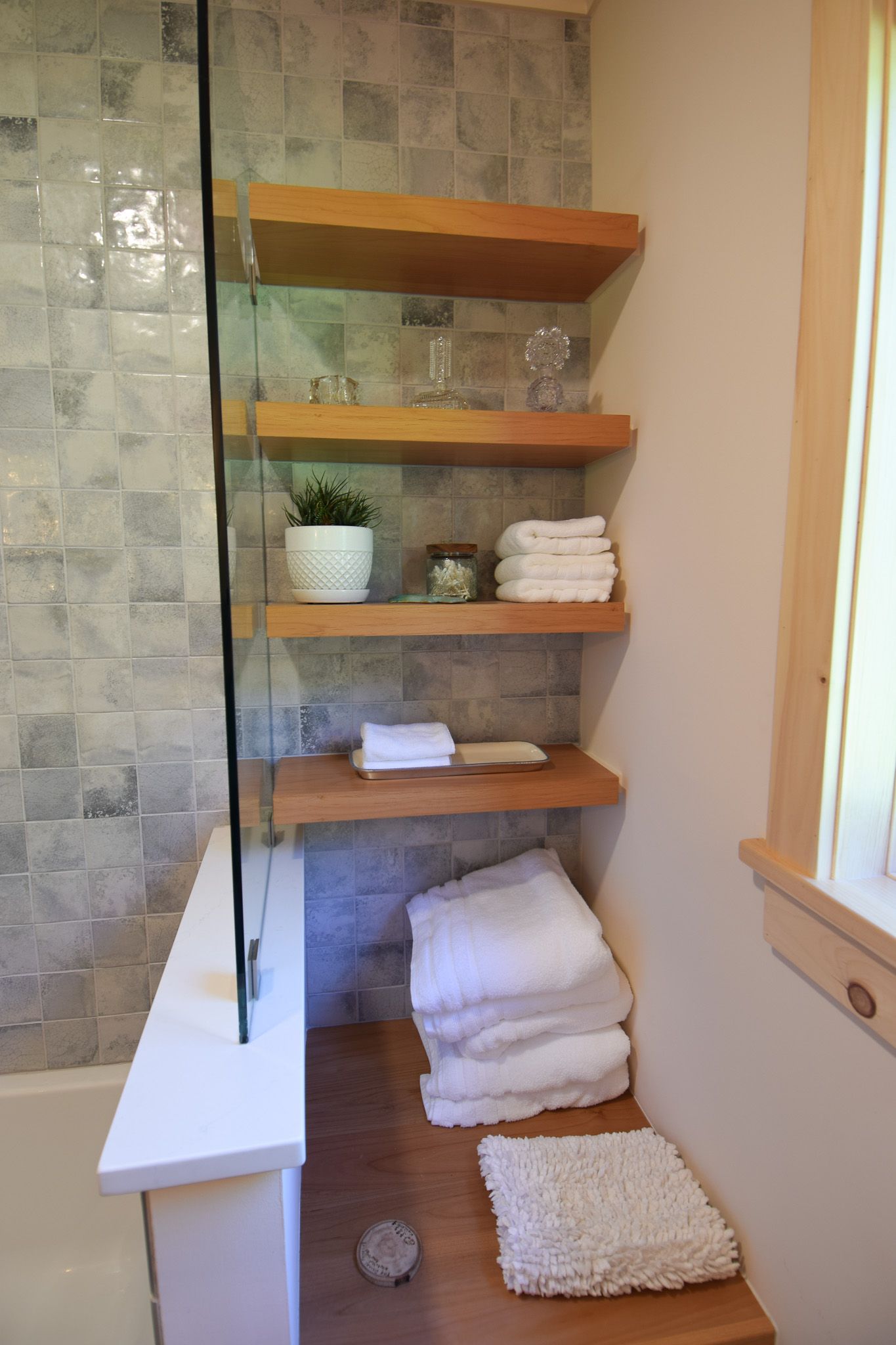 Bathroom shelves with folded white towels, a potted plant, and stone tile shower wall.