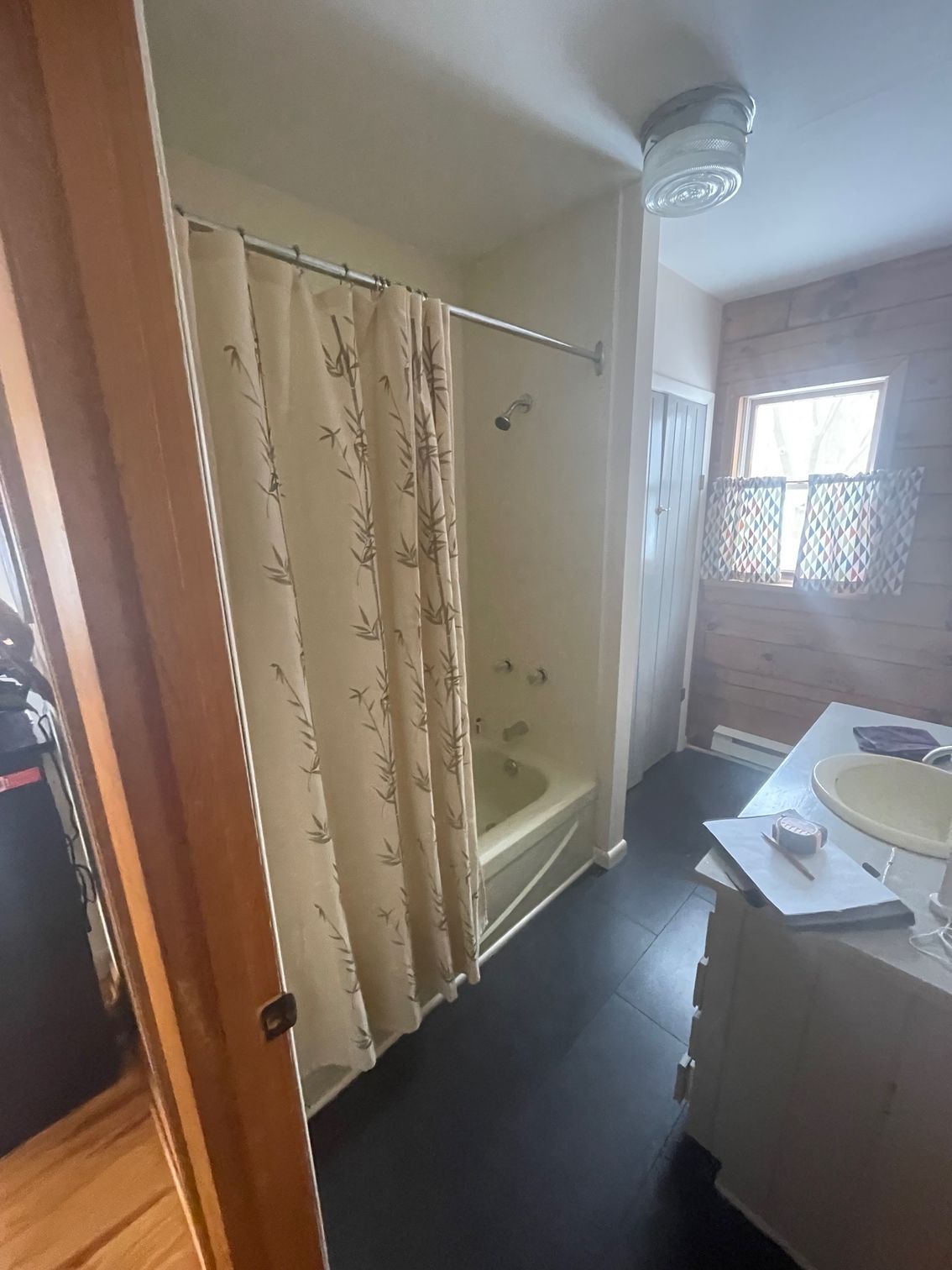 Small bathroom with shower curtain, sink, mirror, and window letting in daylight.