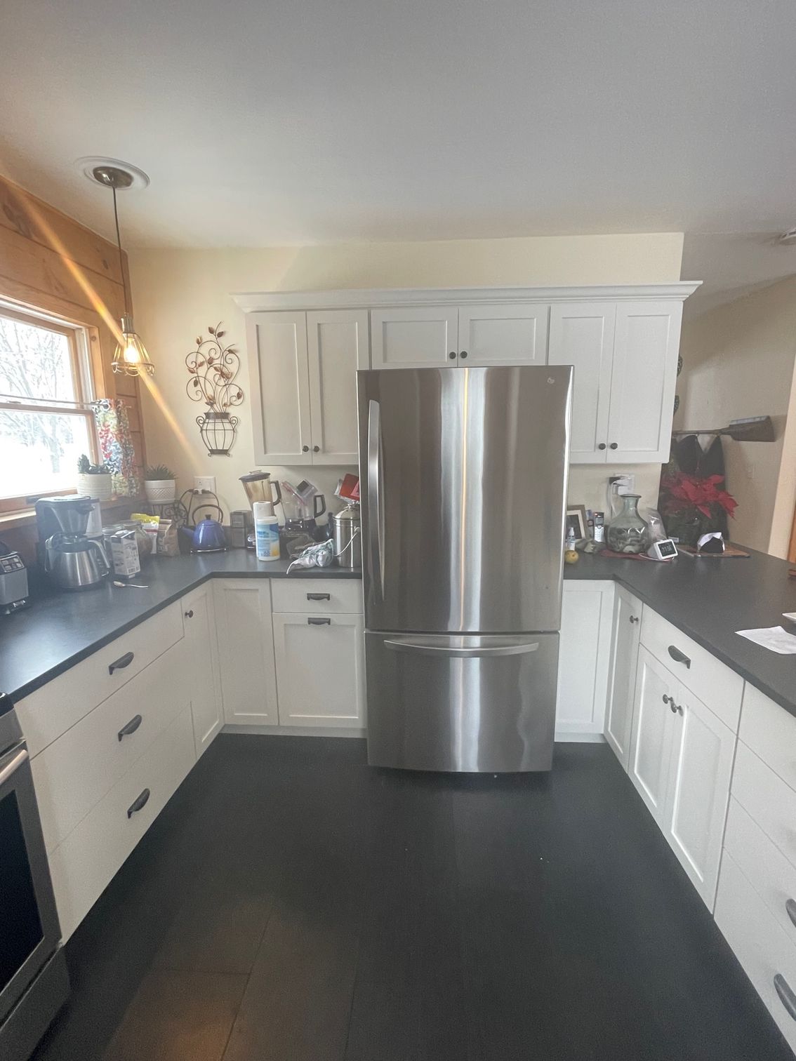 Bright kitchen with white cabinets, stainless steel fridge, dark countertops, and black floor