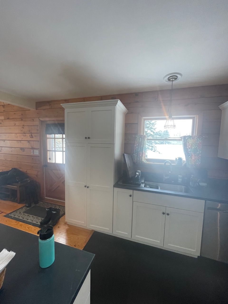 Kitchen interior with white cabinets, a window over the sink, and a black countertop with a teal bottle