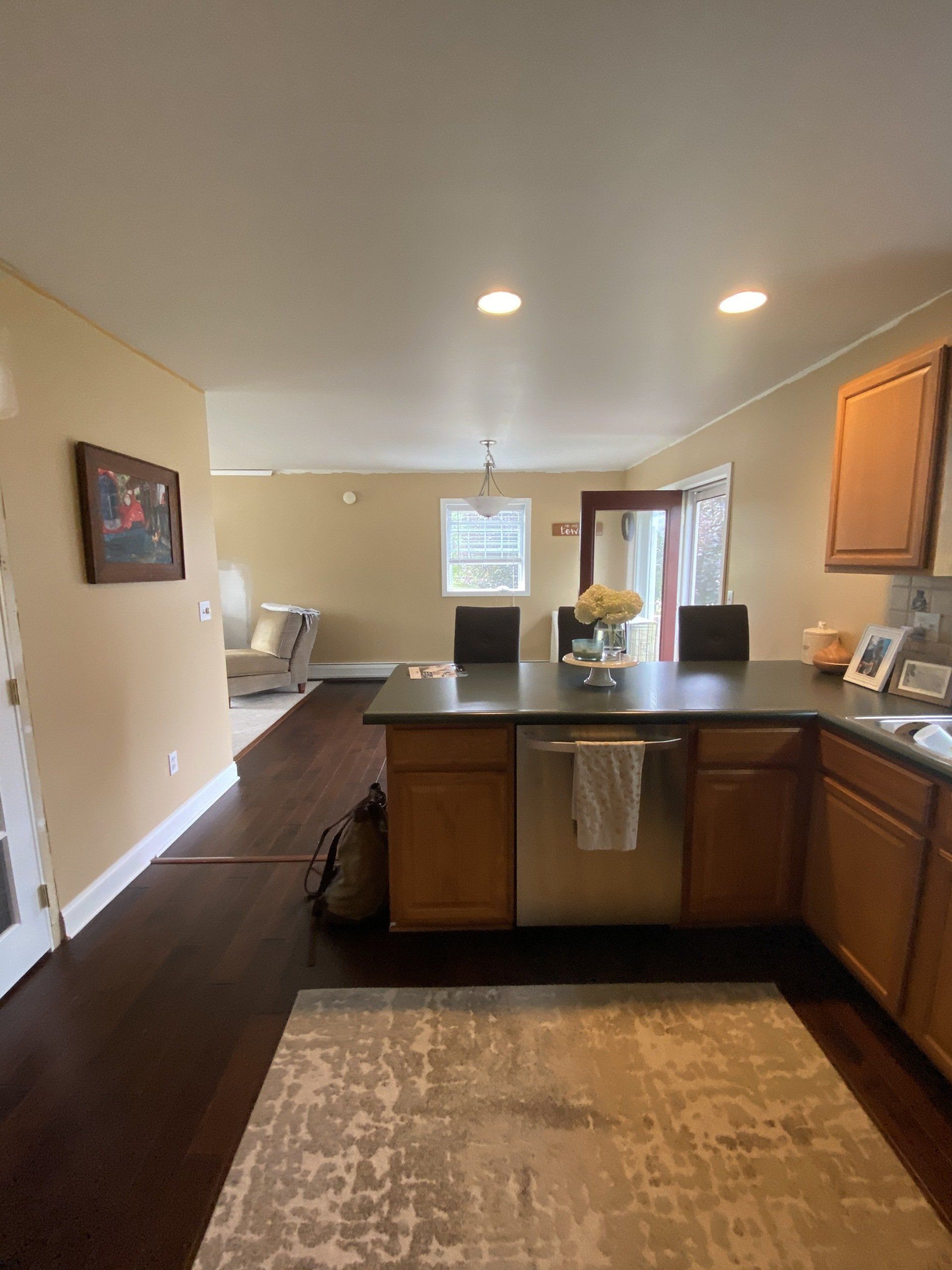 Modern kitchen with island, dark countertops, wood cabinets, beige walls, and a small dining area in the background
