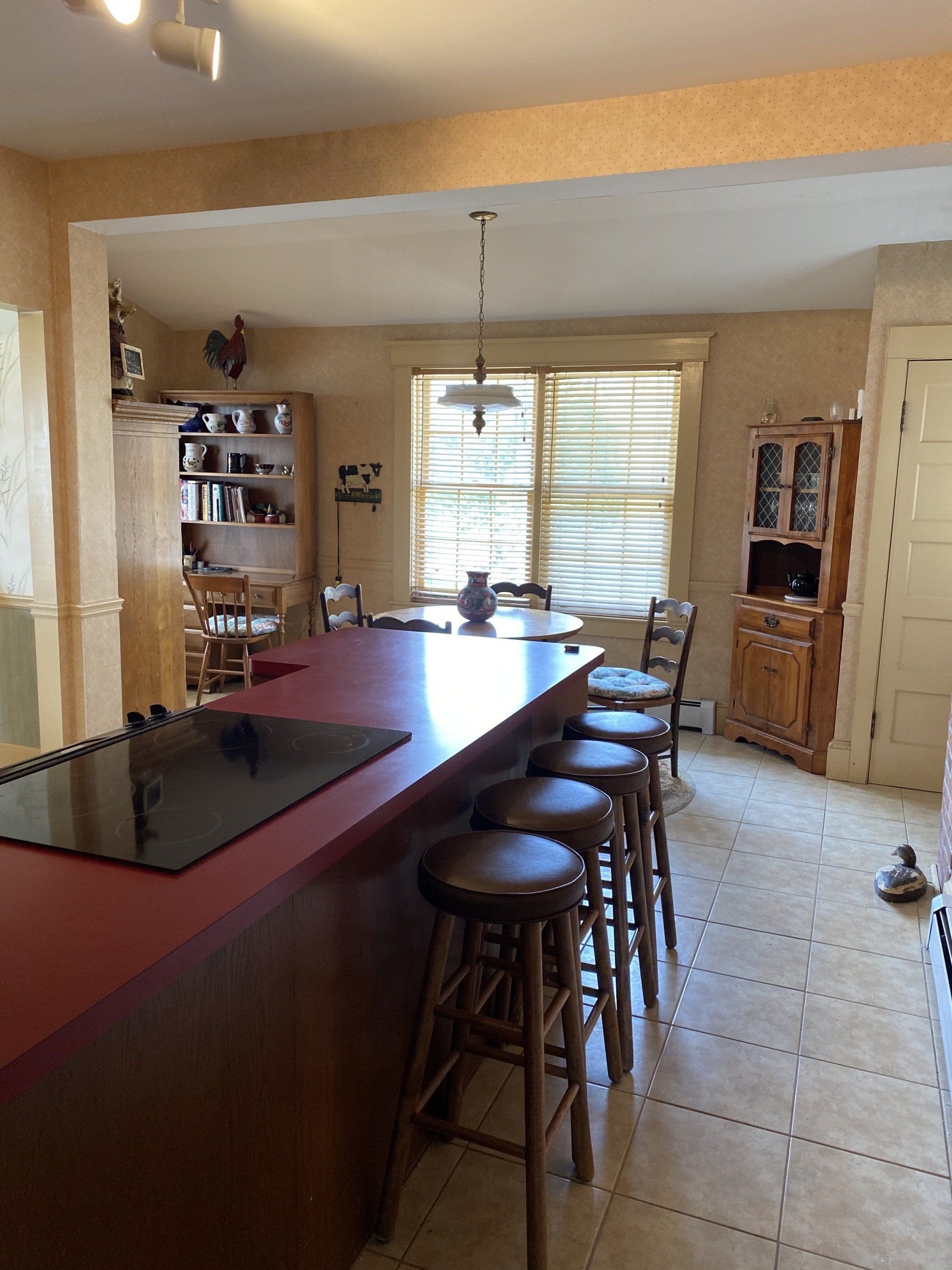 Kitchen with a red island, stools, tiled floor, and bright window blinds at the back.