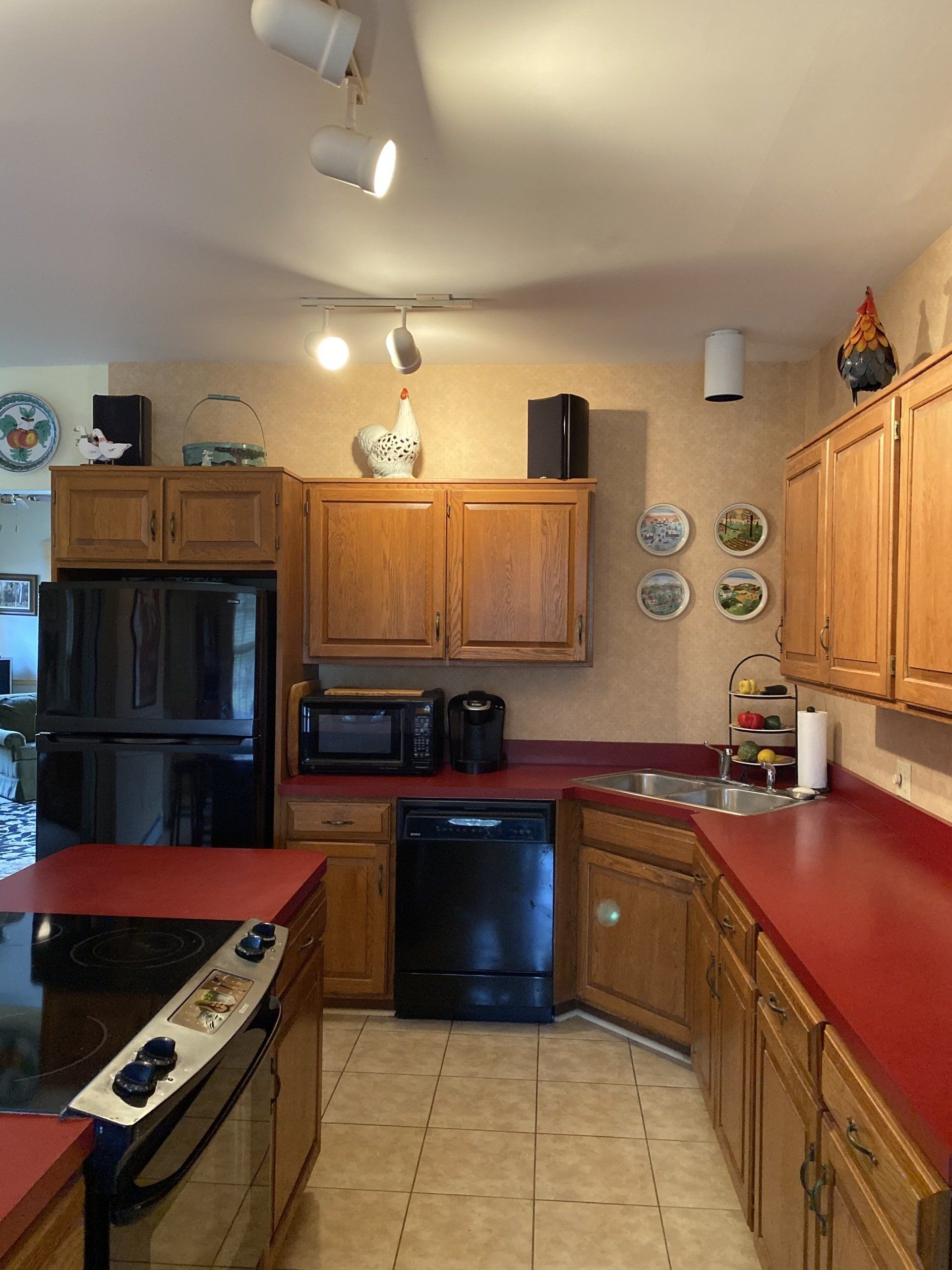 Kitchen with wooden cabinets, red countertops, black appliances, and decorative plates on a beige tile floor.