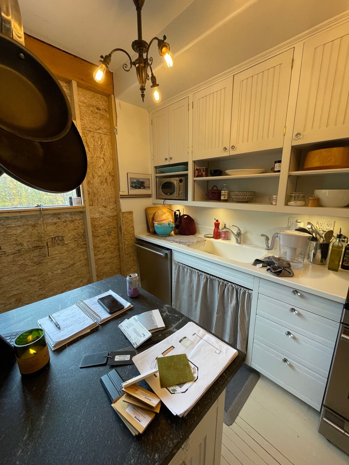 Cozy rustic kitchen with white cabinets, open shelves, hanging lights, and a table with books and papers