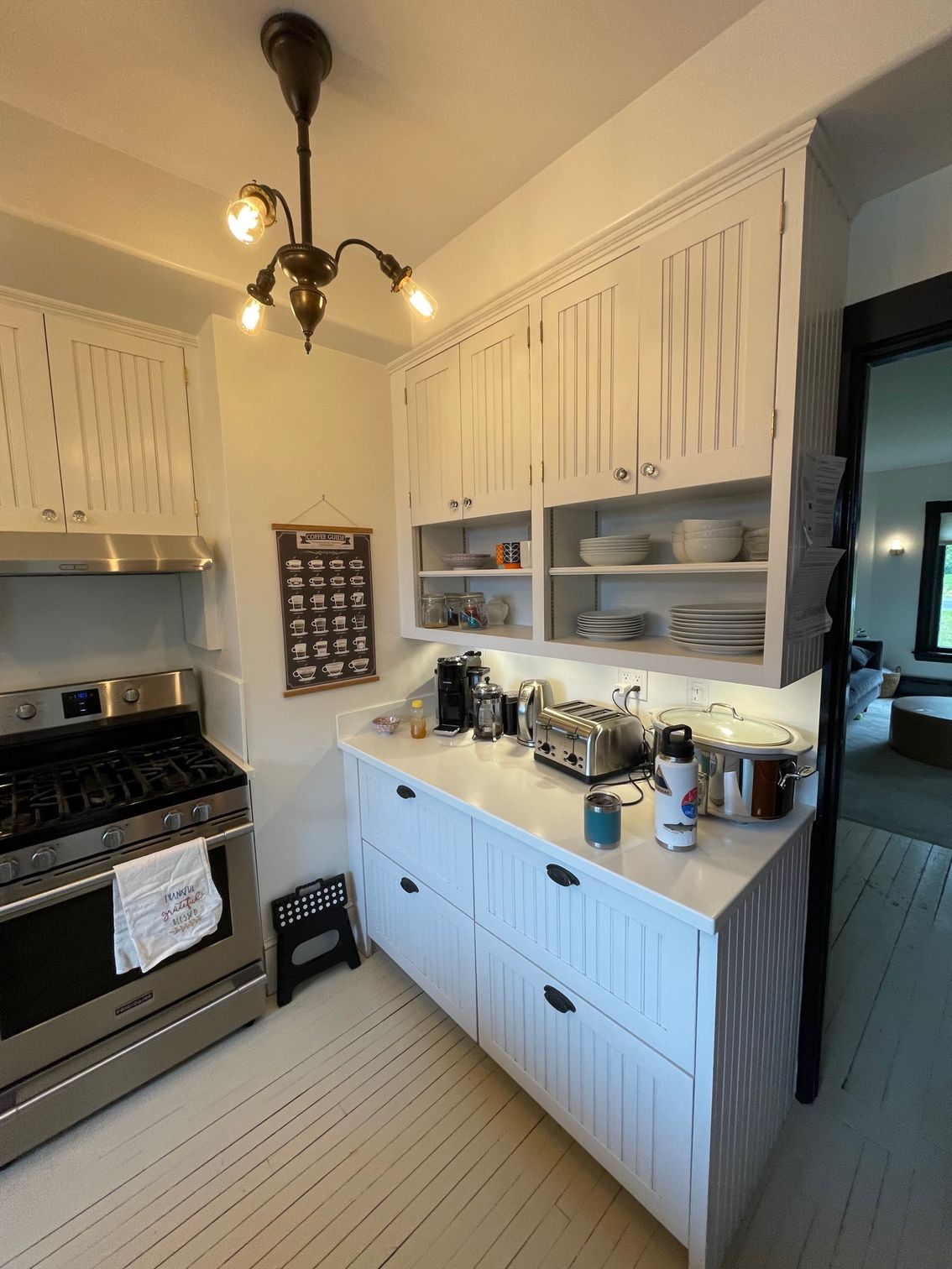 Small vintage kitchen with white cabinets, black stove, open shelves, and a central island.