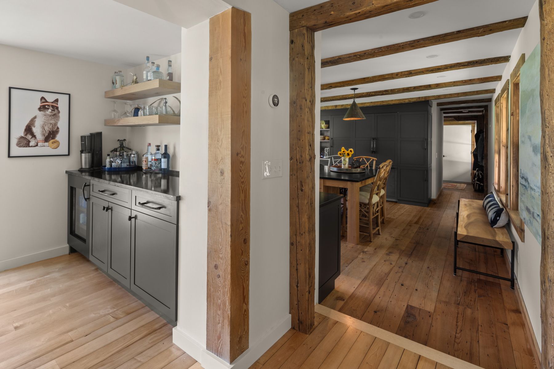 Narrow hallway with rustic wood beams, gray kitchenette, and a view into a cozy wooden dining area