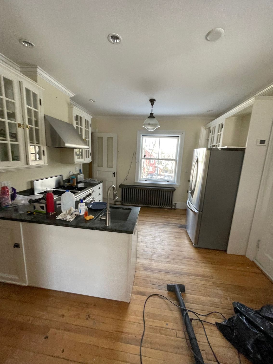 Bright kitchen with white cabinets, wood floors, stainless fridge, and a window at the far end.