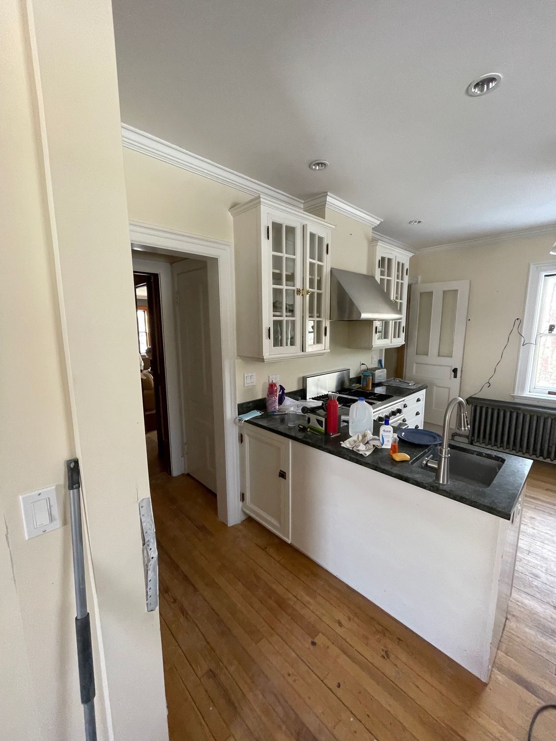 Bright kitchen with white cabinets, dark countertops, wood floor, and a central island near a hallway.