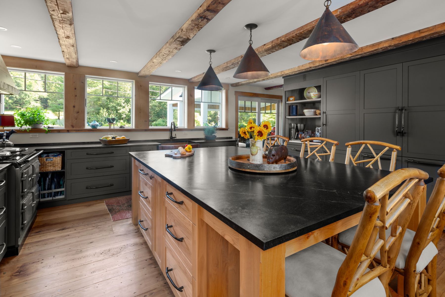 Modern kitchen with dark cabinets, large island, and wood ceiling beams under hanging pendant lights