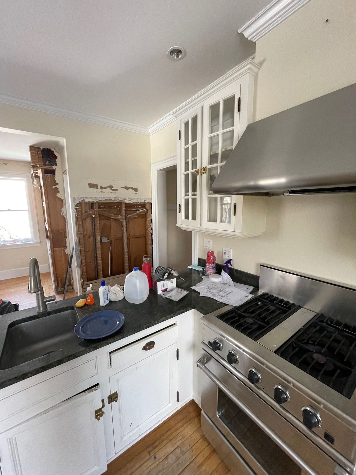 Kitchen with stainless steel stove and hood, white cabinets, black countertop, and dishes by the sink
