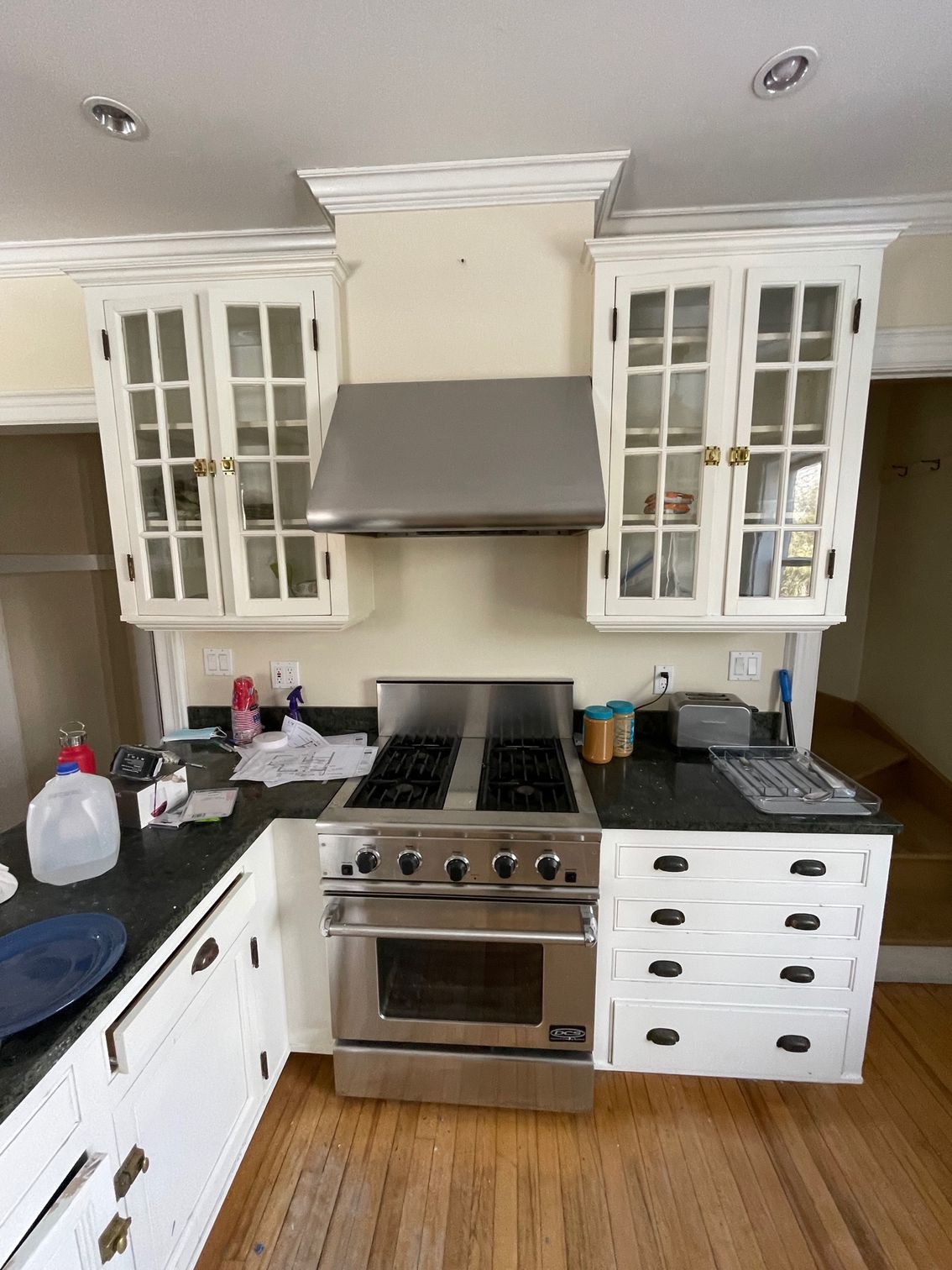 Compact kitchen with white cabinets, stainless steel stove, gray range hood, and black countertops.