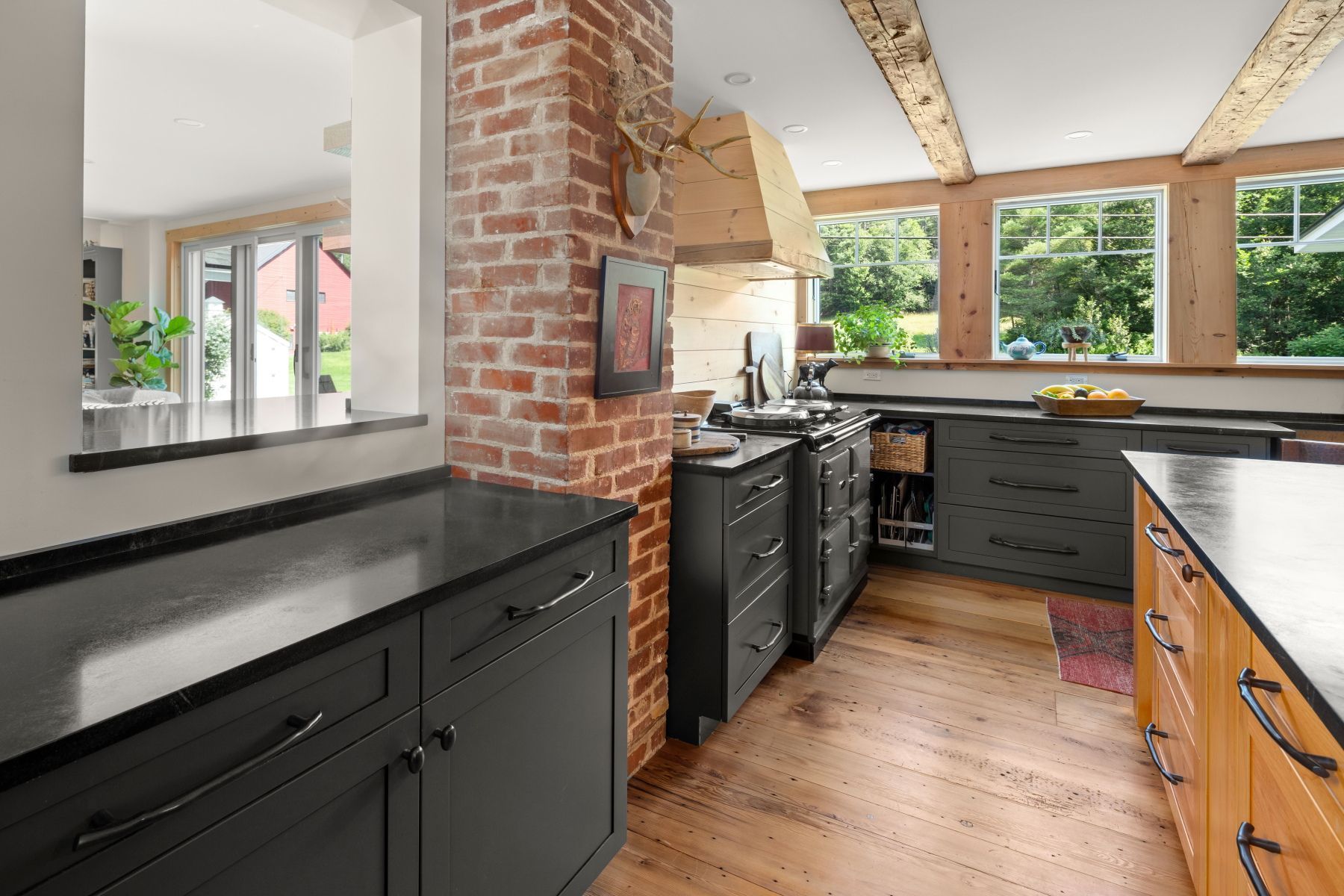 Modern kitchen with black cabinets, brick wall, wood floors, and large windows overlooking greenery
