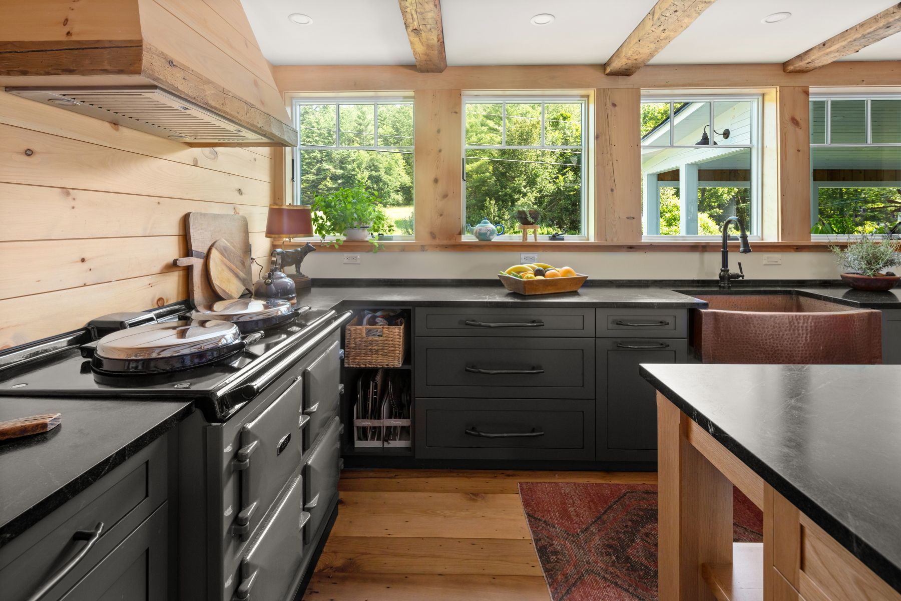 Modern kitchen interior with dark cabinets, wood ceiling, and large windows overlooking greenery
