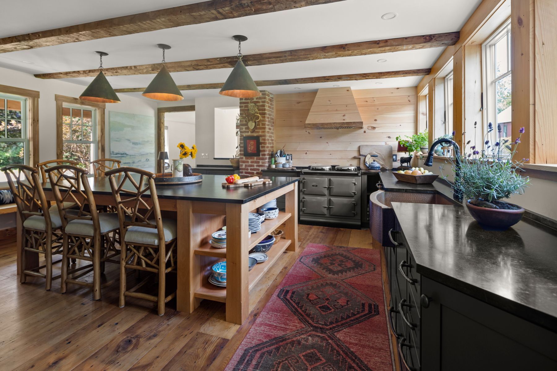 Bright rustic kitchen with island, pendant lights, wooden beams, and a stove against the back wall.