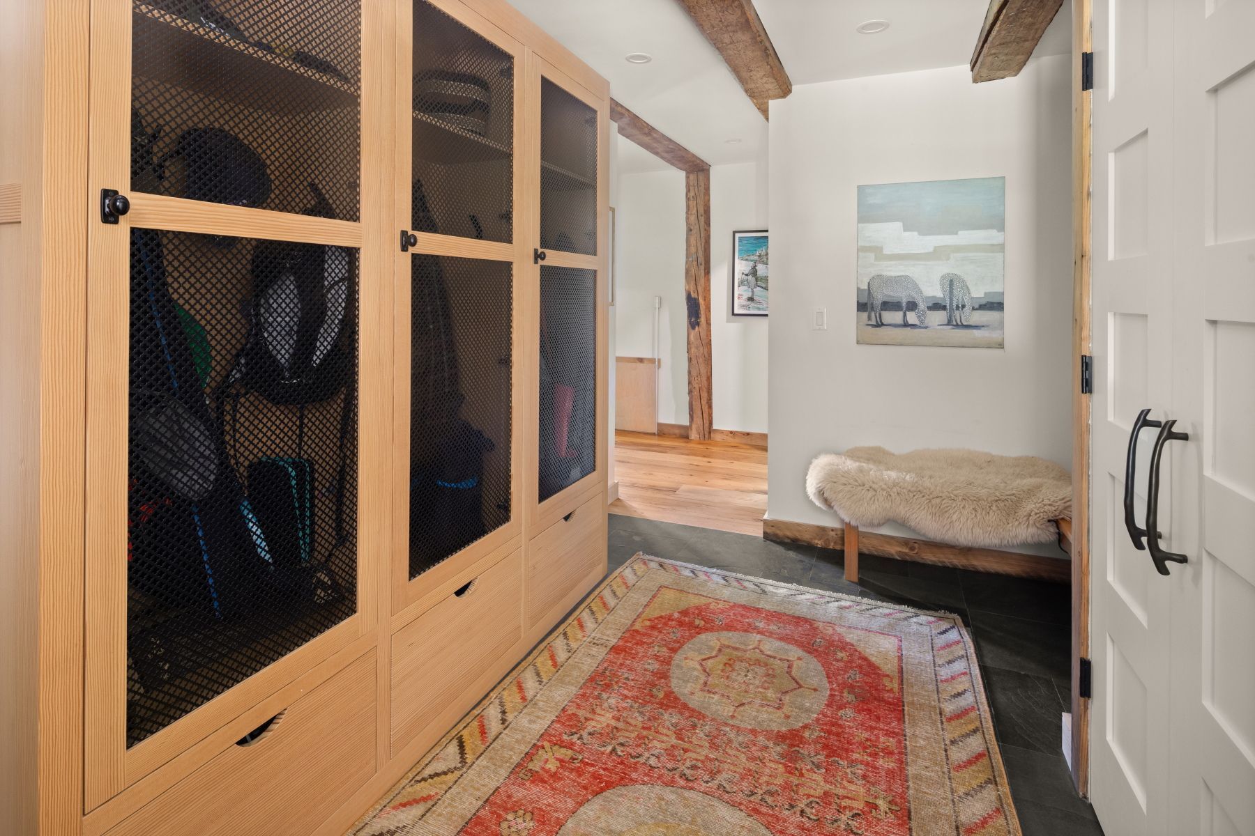 Hallway with wooden dog crates, patterned rug, bench, and open doorway leading to a bright room