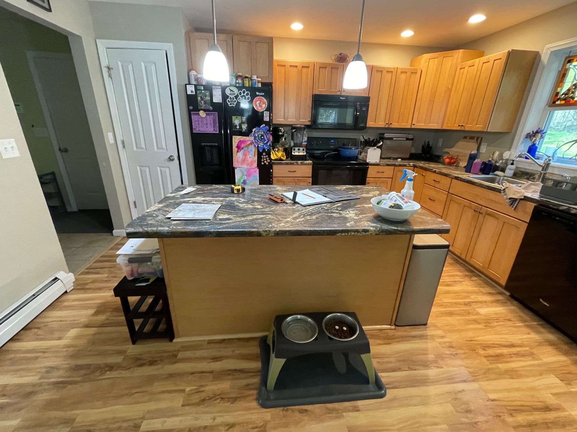 Kitchen with island, wood cabinets, black appliances, and pet bowls on the floor.
