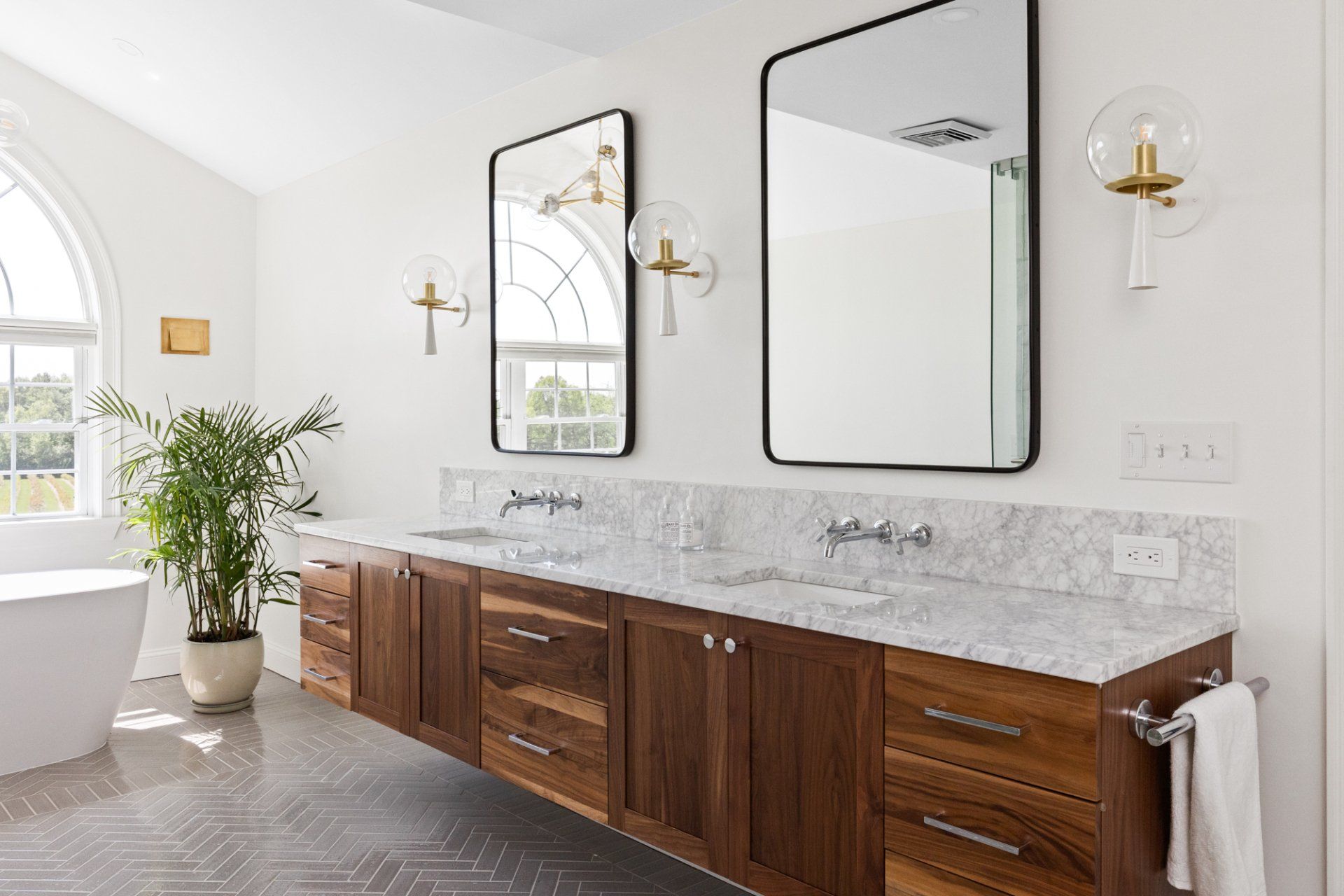 Modern bathroom with double vanity, large mirrors, marble countertop, and potted plant by a tub.