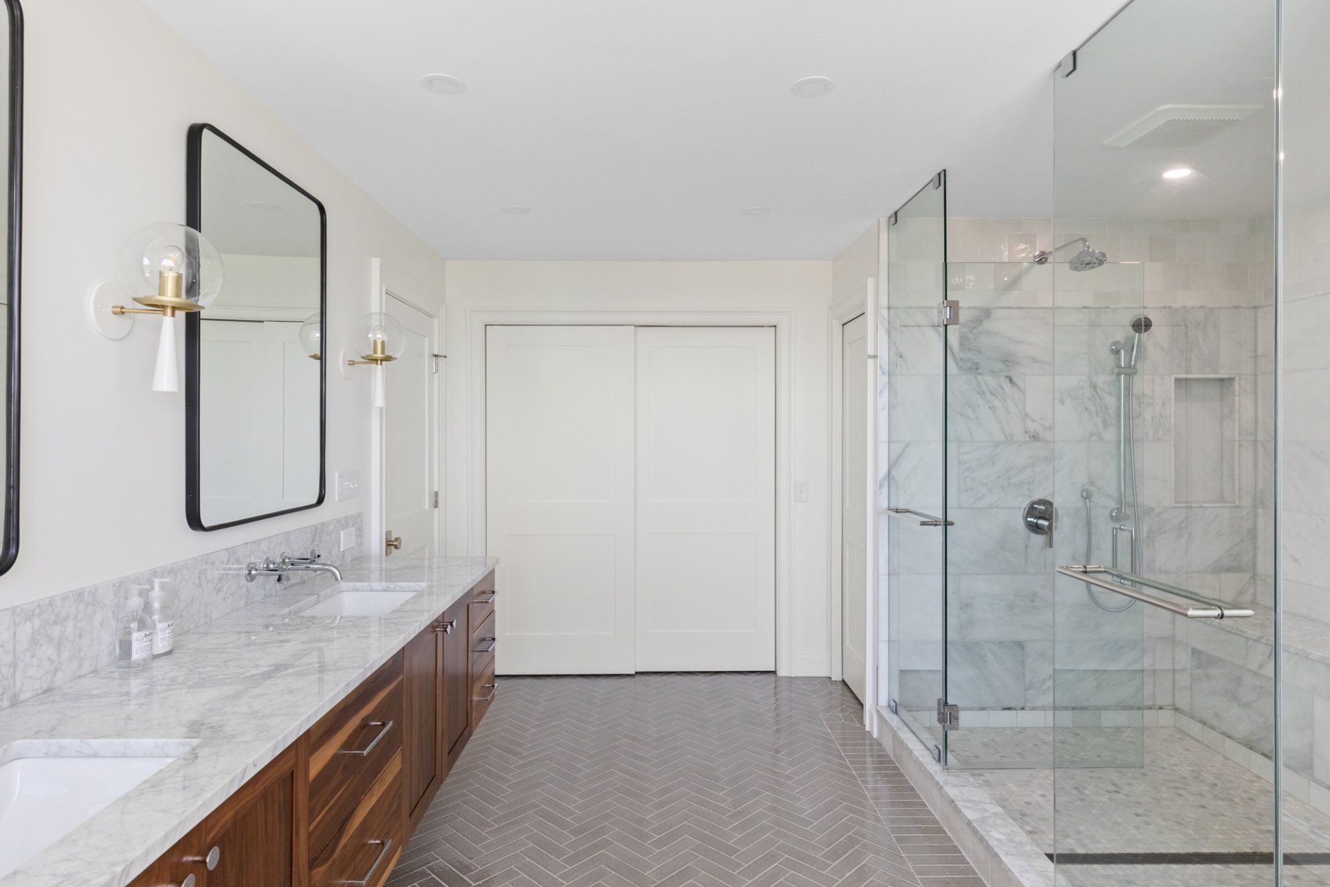 Bright modern bathroom with marble vanity, double mirrors, glass shower, and white double doors