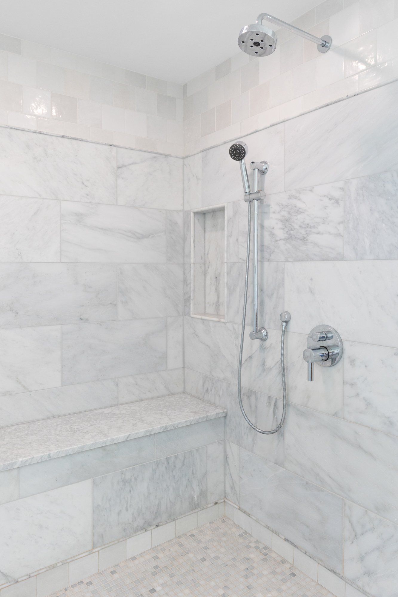 White marble-tiled walk-in shower with bench, handheld shower, and chrome fixtures