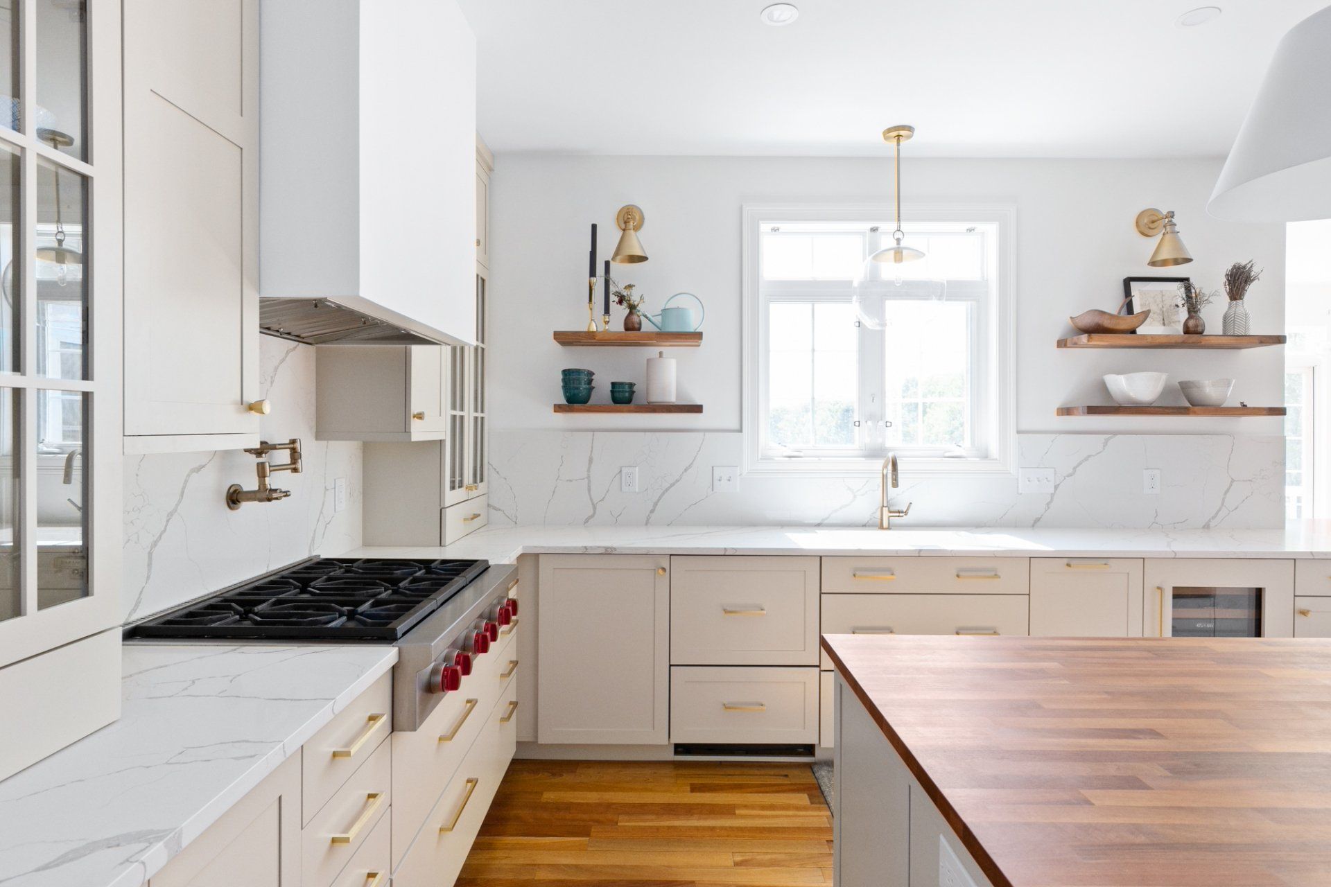 Bright white kitchen with wood island, gas range, and open shelves by a sunlit window