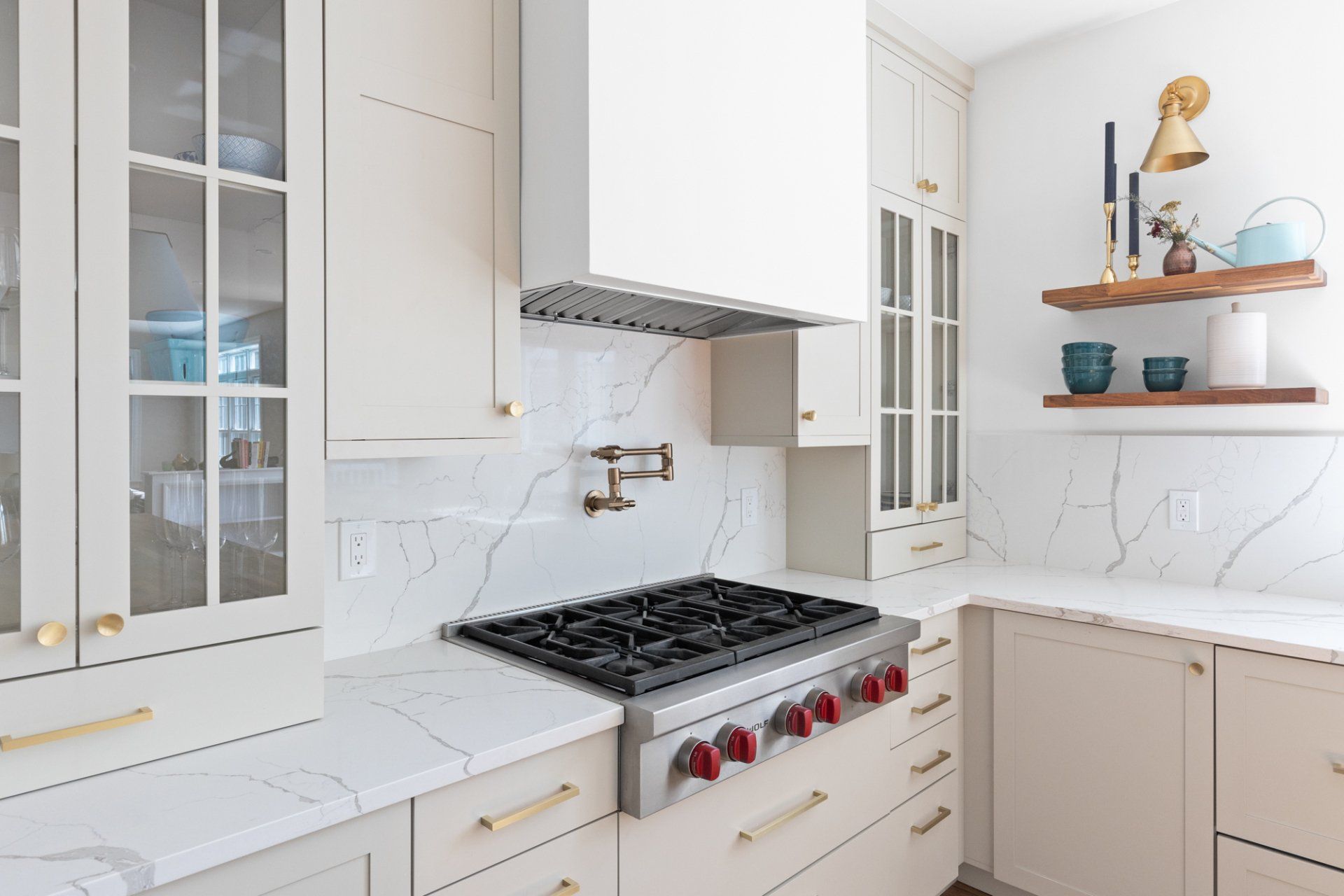 Bright white kitchen with marble countertops, gas range, and open shelves with decor
