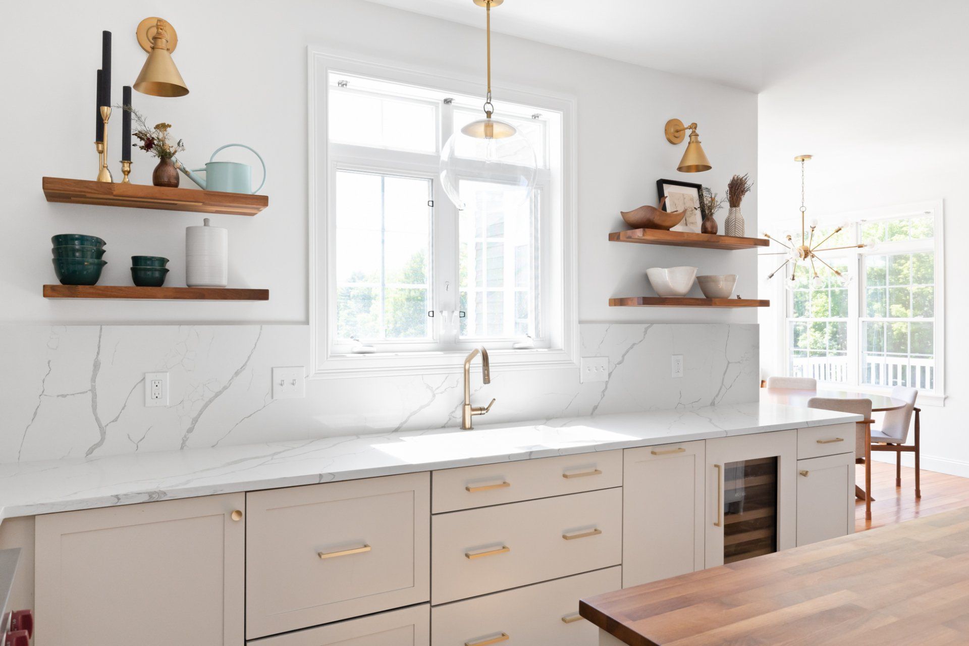 Bright white kitchen with wooden shelves, marble backsplash, and a large window above the sink.