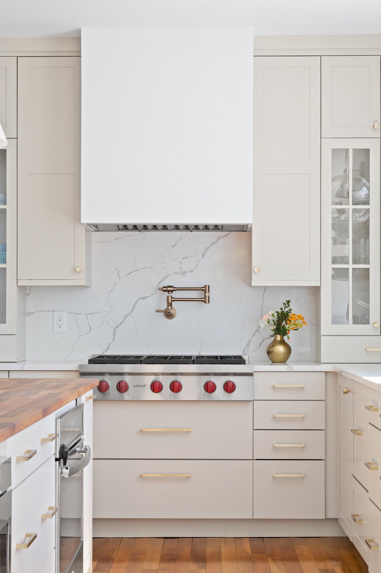 Bright white kitchen with marble backsplash, brass faucet, gas range, and red knobs