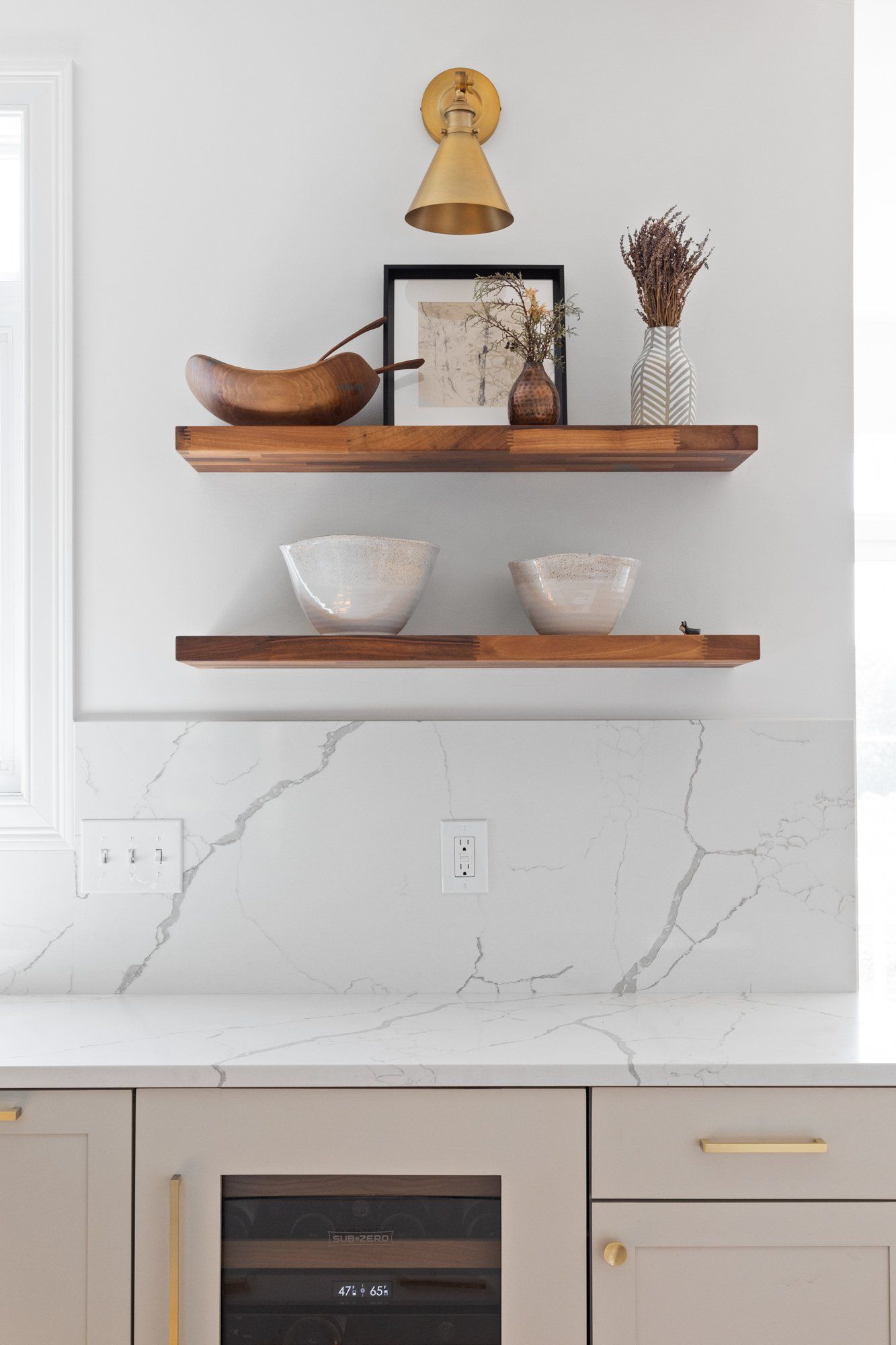 Minimal kitchen shelves with wooden decor, bowls, and a white marble backsplash above gray cabinets