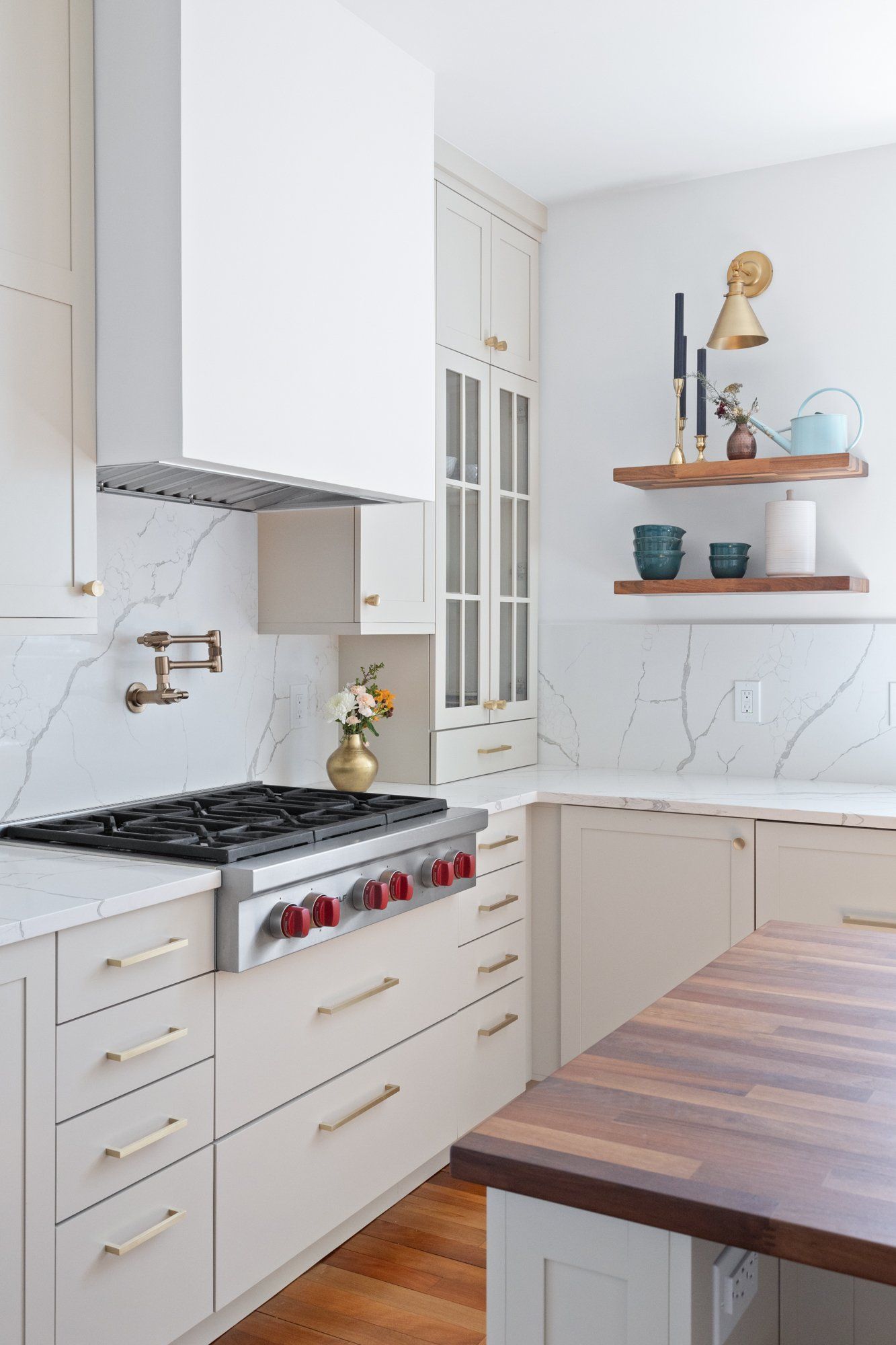 Bright white kitchen with stove, marble backsplash, open shelves, and a wooden table in the foreground