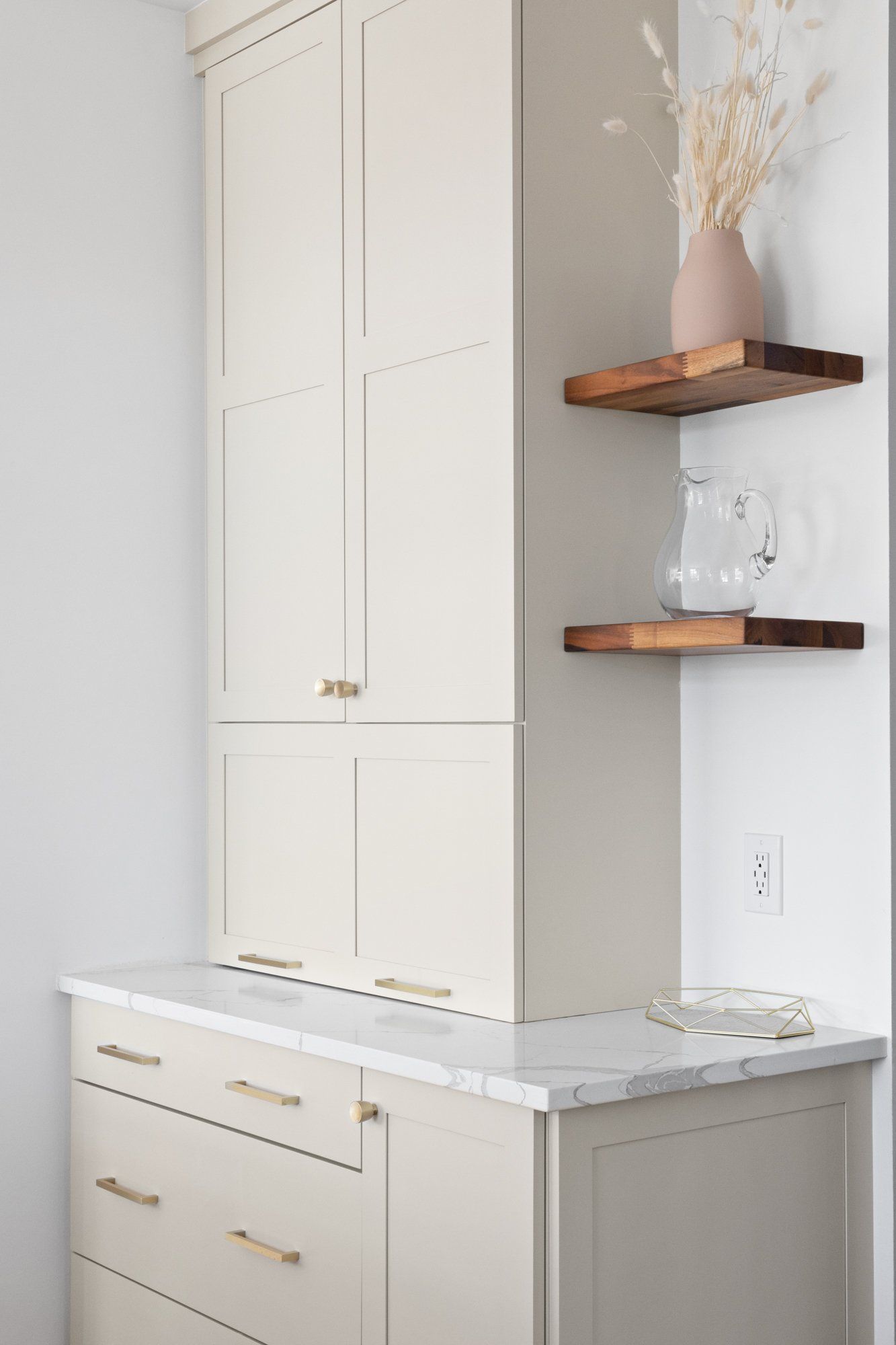 Built-in white cabinets and marble countertop beside wall shelves with vase and glass decor